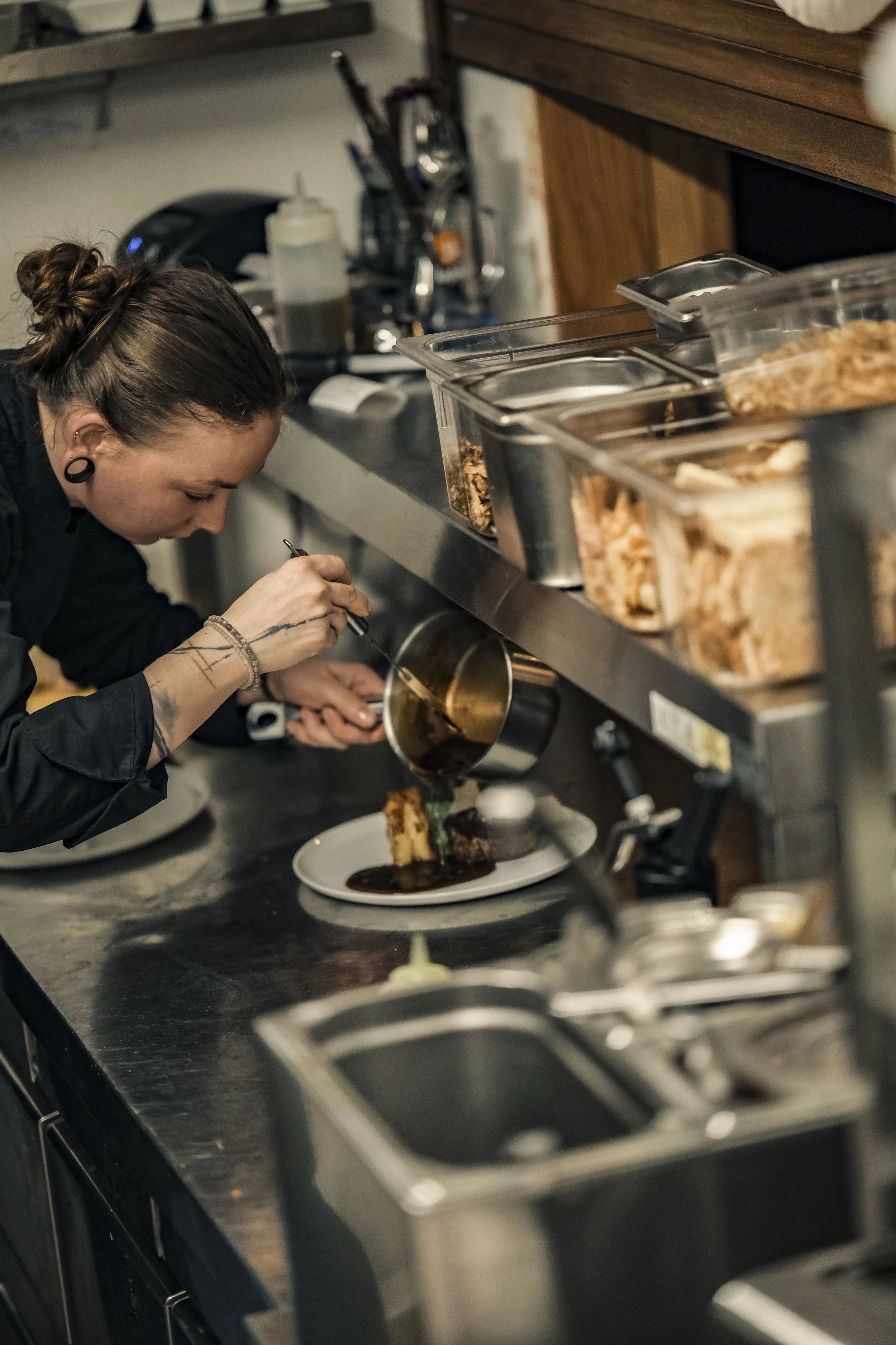 A female chef plating a dessert with chocolate sauce in a professional kitchen.