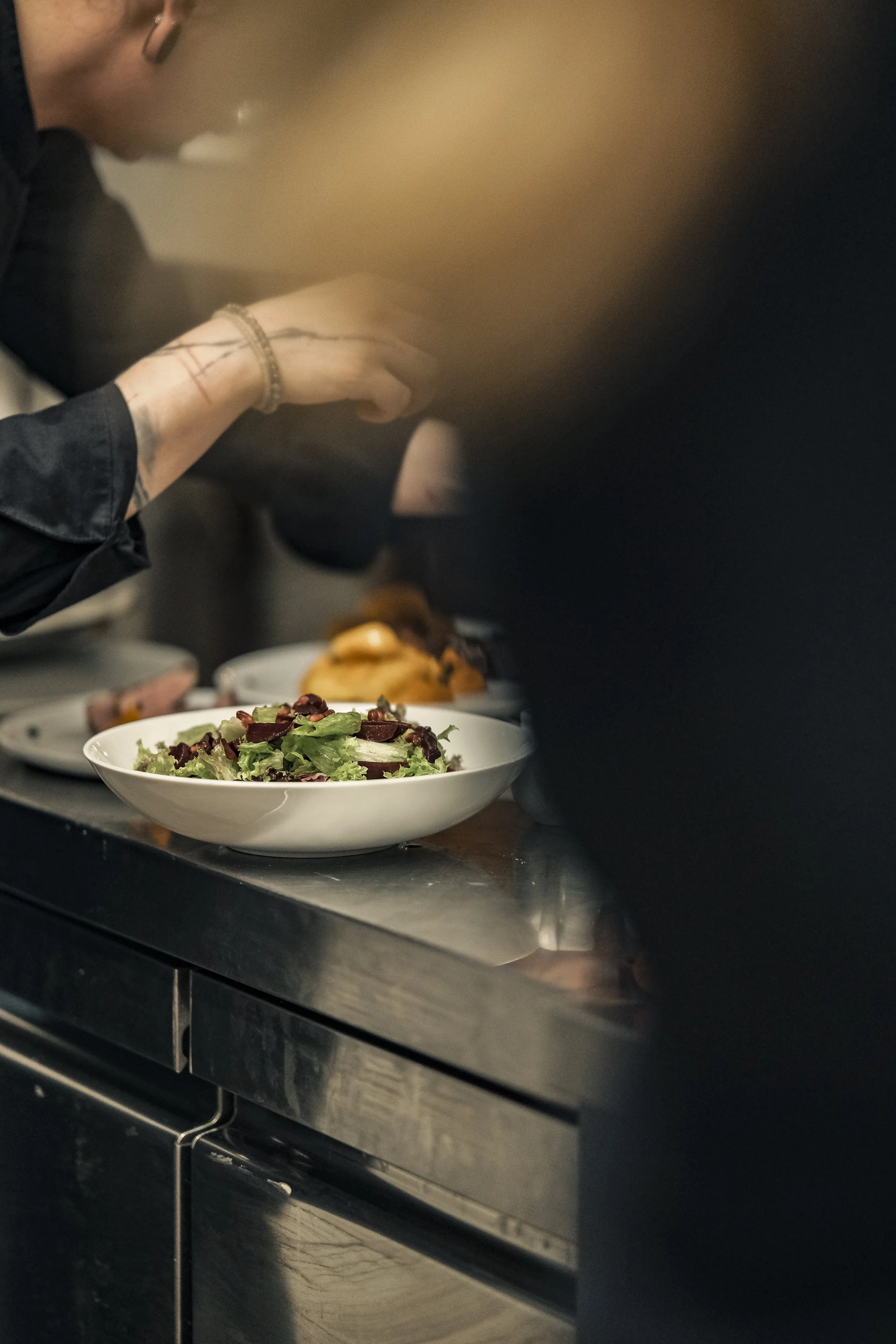 A person preparing a salad in a kitchen with a bowl of fresh greens, chopped vegetables, and other ingredients on the counter.