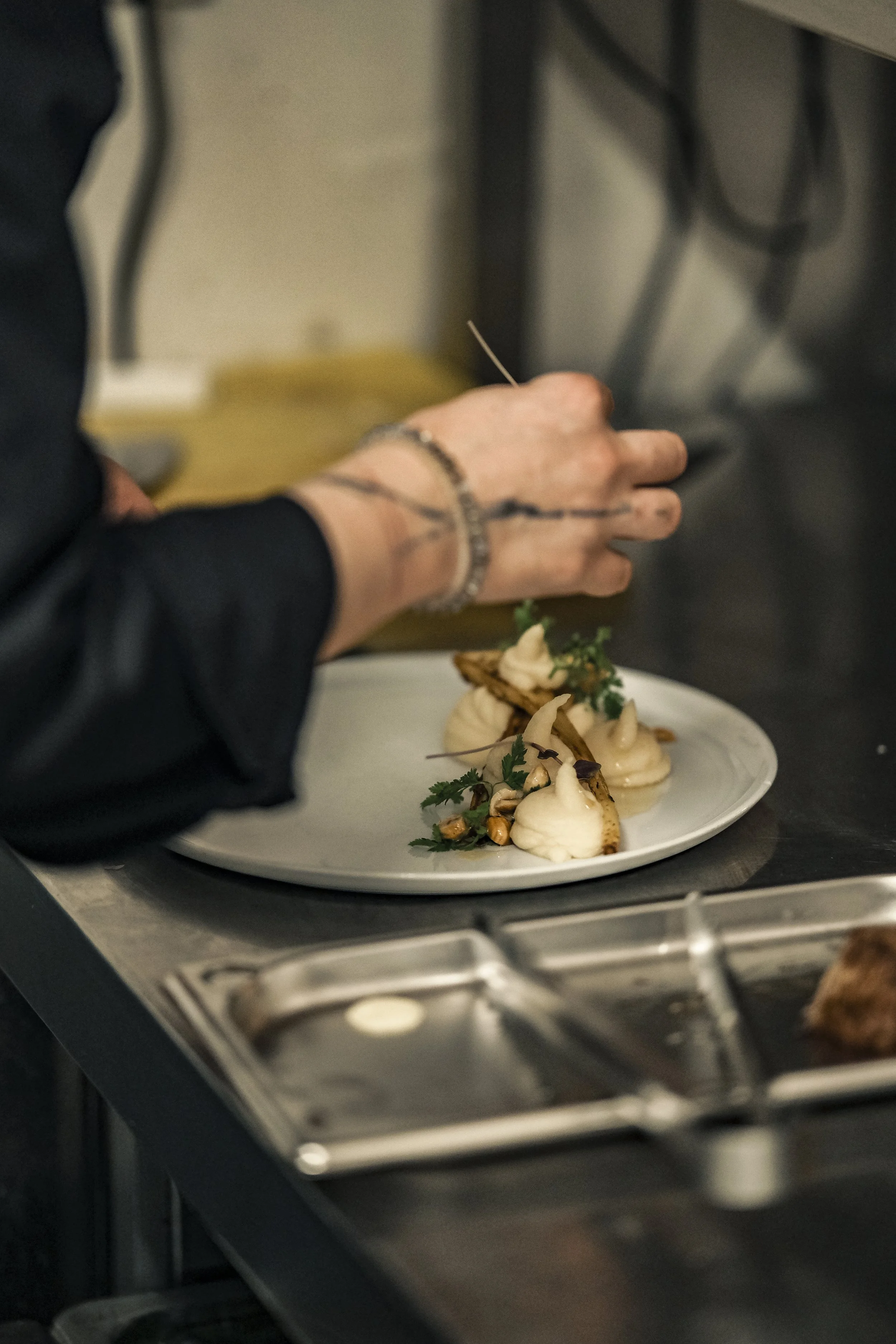 Chef garnishing a plated dish with herbs in a professional kitchen.