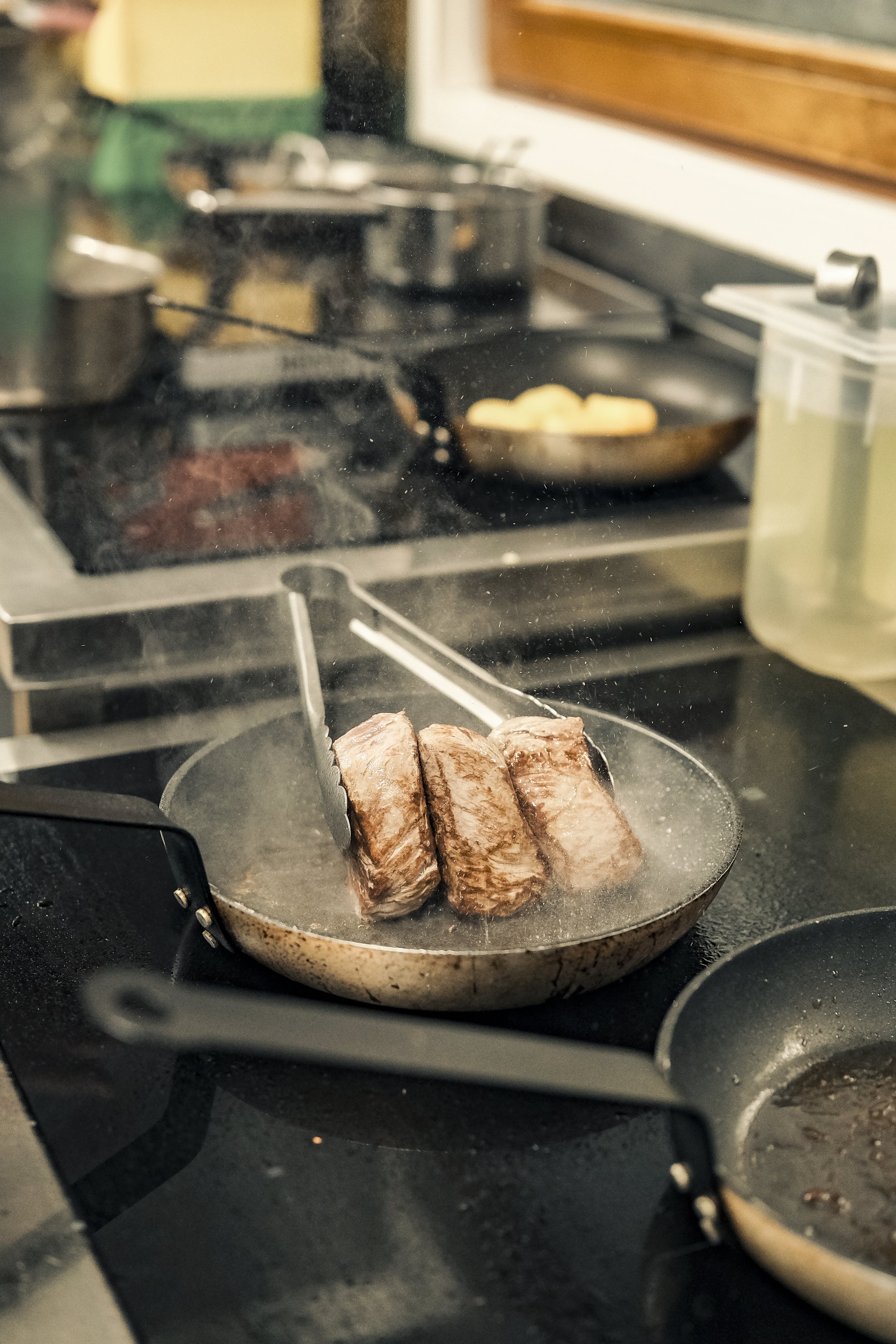 Three pieces of meat cooking in a frying pan on a stovetop.