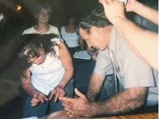 A man demonstrating or demonstrating something to a group of women, with some women watching intently and one woman smiling in the background.