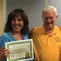 A woman holding a certificate standing next to an older man in a yellow shirt, both smiling.