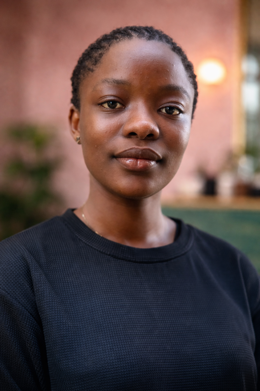Close-up portrait of a young African American woman with short natural hair, wearing a black athletic shirt, standing indoors with a softly blurred background.