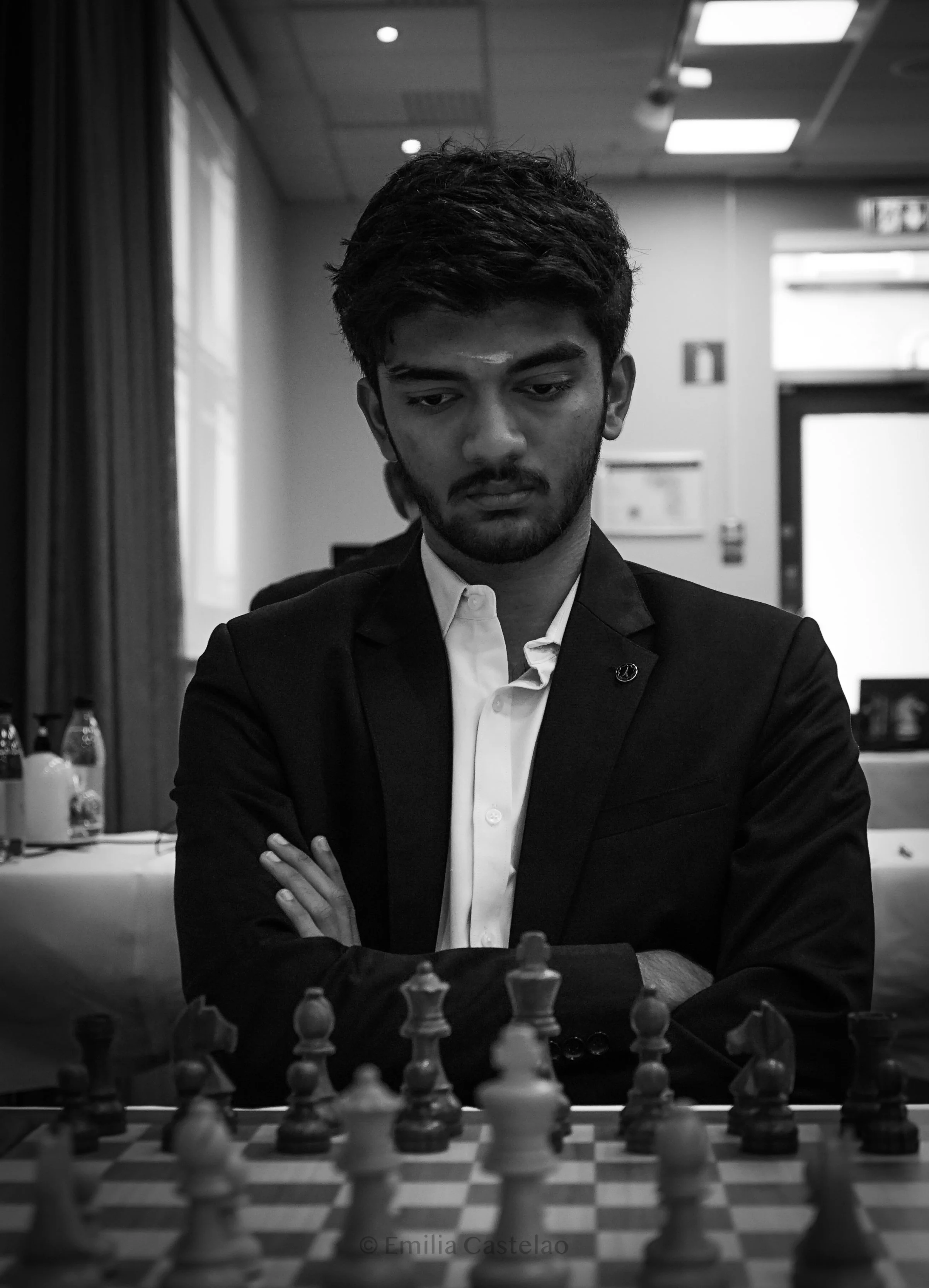 A young man in a suit playing chess indoors, with a thoughtful expression on his face.