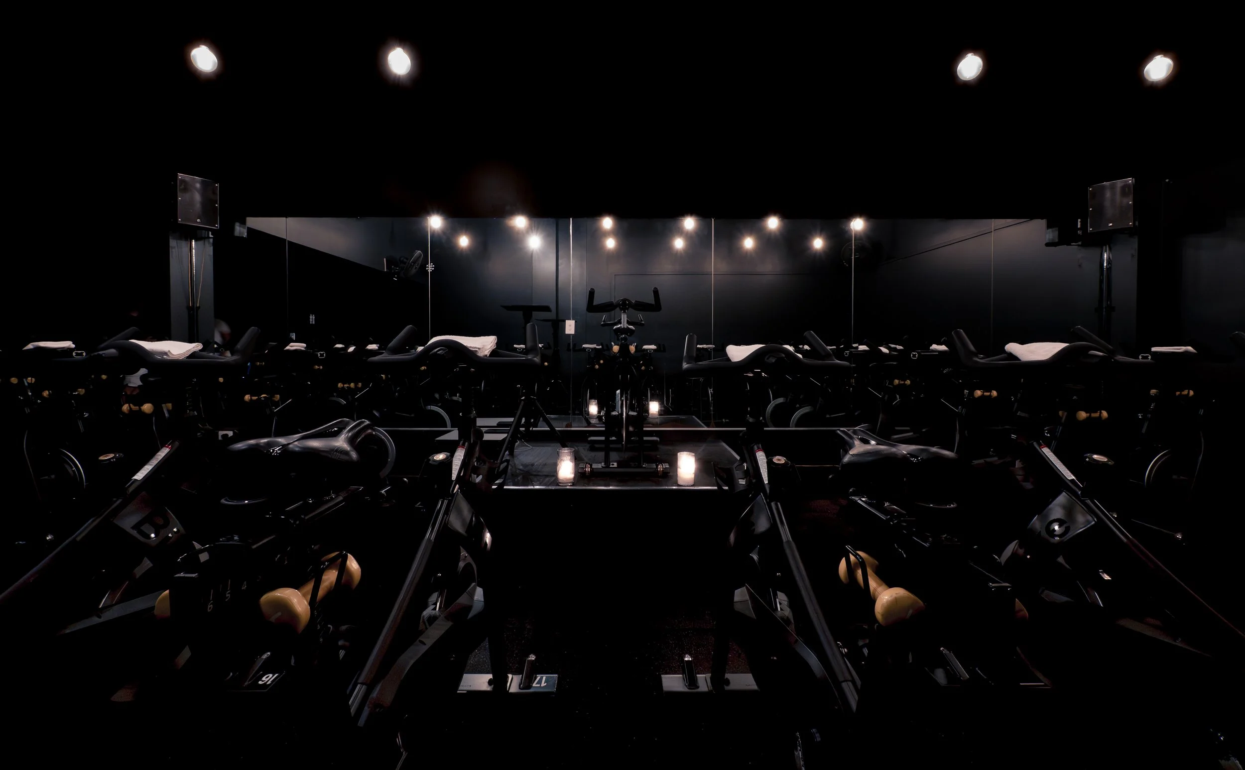 Darkly lit fitness studio with exercise bikes arranged in rows, large mirror on the wall, and soft lighting creating a calming atmosphere.