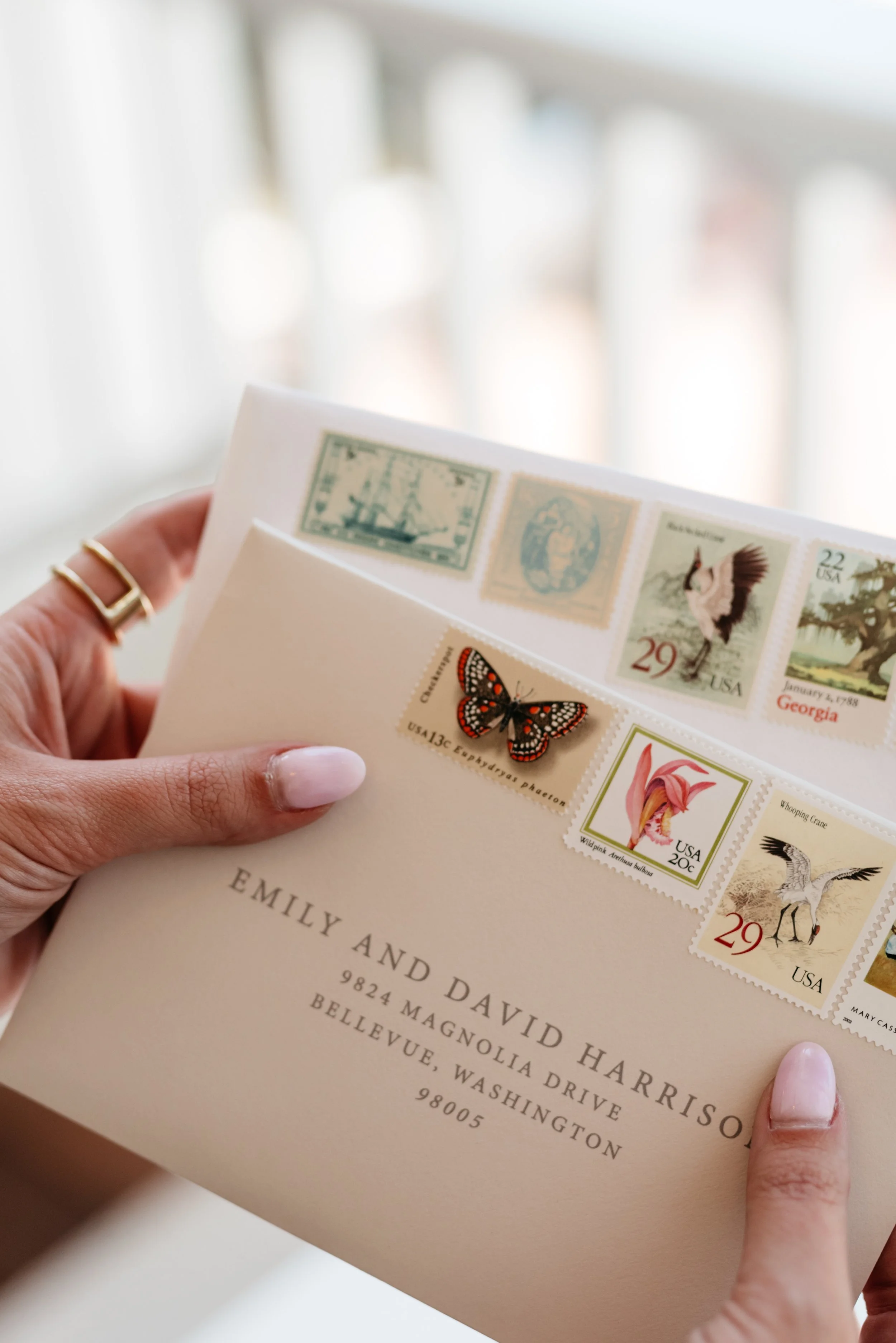 Hands holding addressed envelopes with vintage stamps, featuring butterfly and crane images, in Bellevue, Washington.