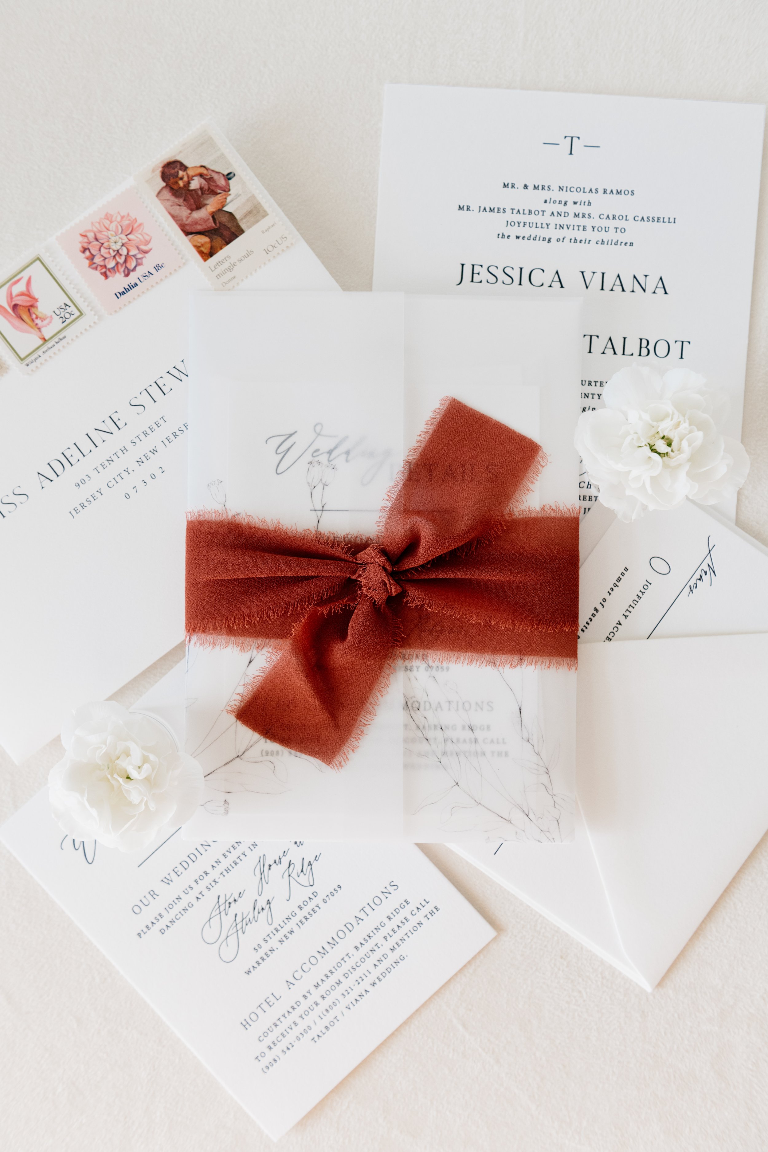 Elegant wedding invitation set with white and burgundy details, featuring a ribbon and floral decoration.