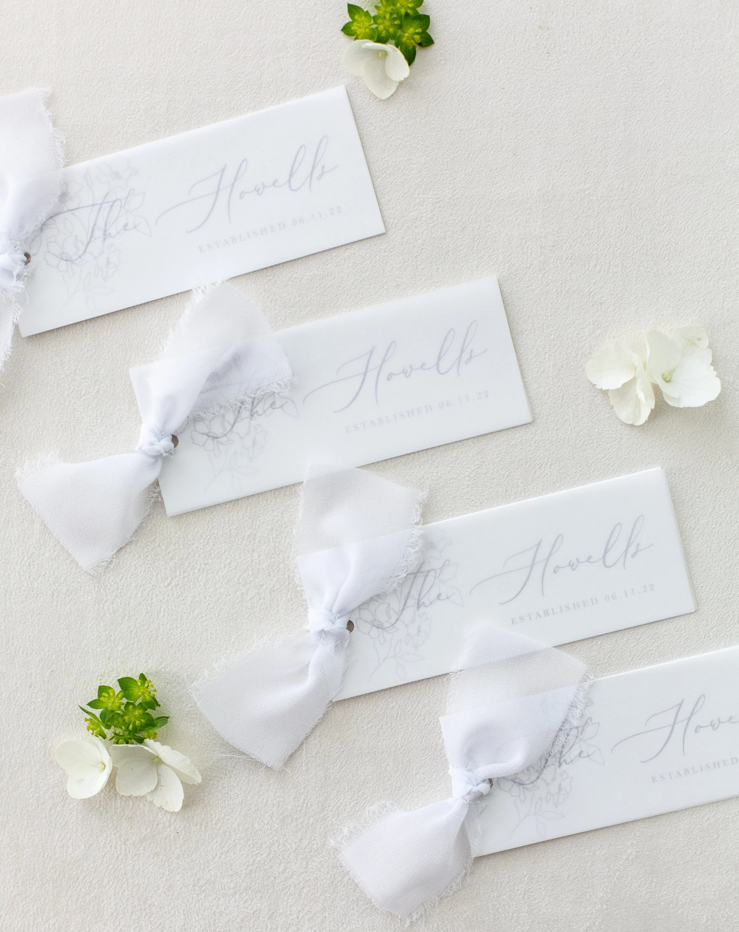 Wedding place cards with white ribbon bows and floral design on a light background, surrounded by small white and green flowers. Newport, Rhode Island