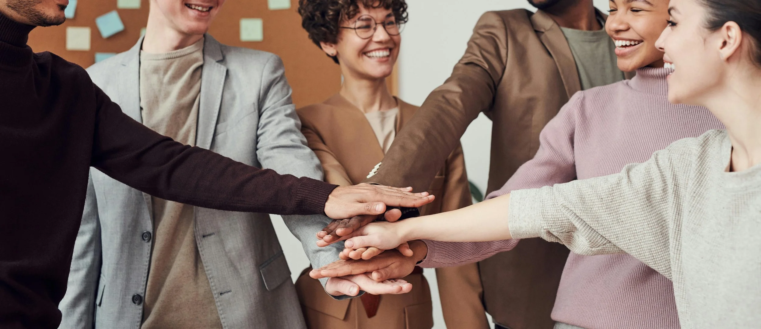 A diverse group of six people in business attire engaging in a team-building activity, stacking their hands together in a show of unity and collaboration.