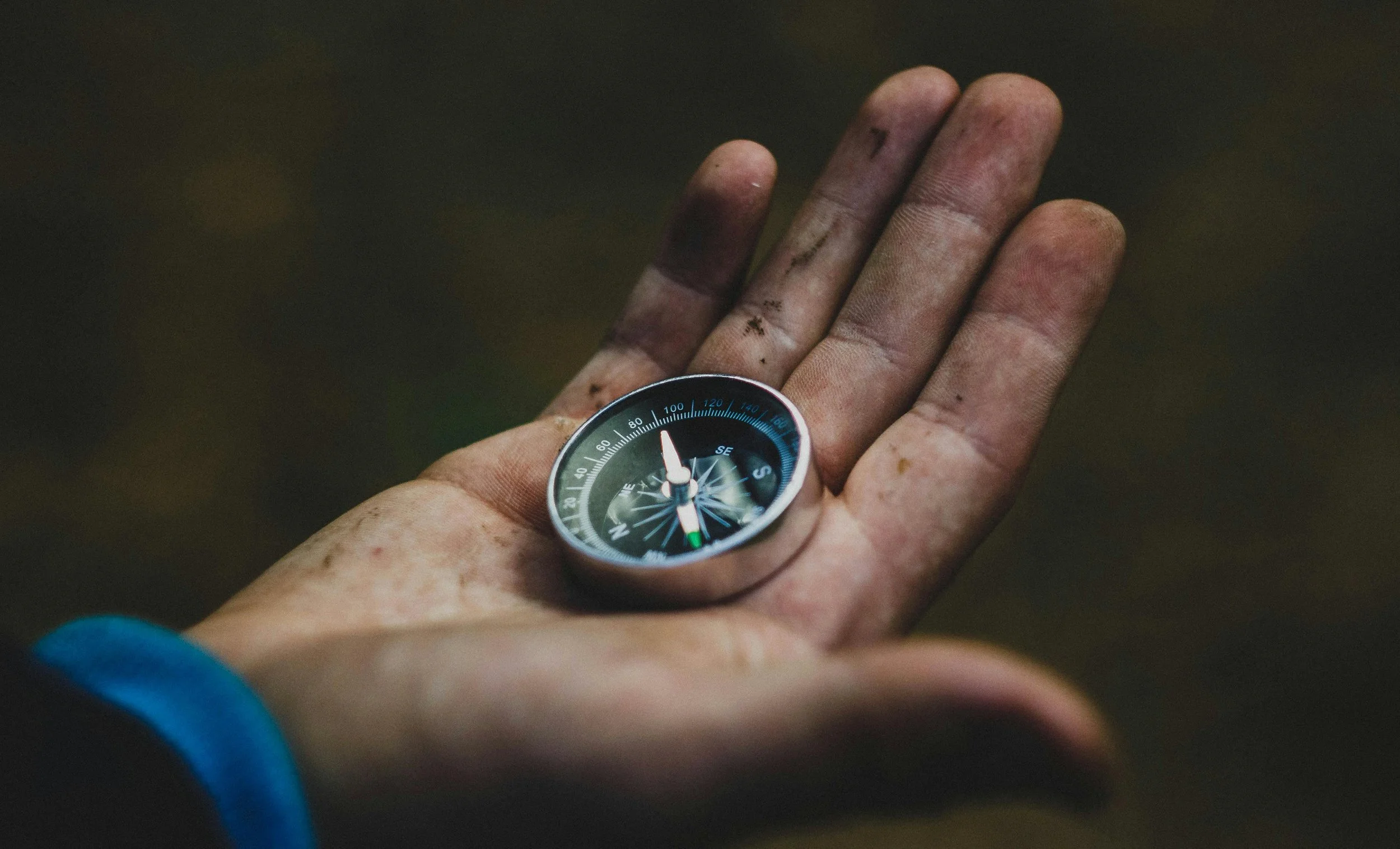 A dirty, muddy hand holding a compass.