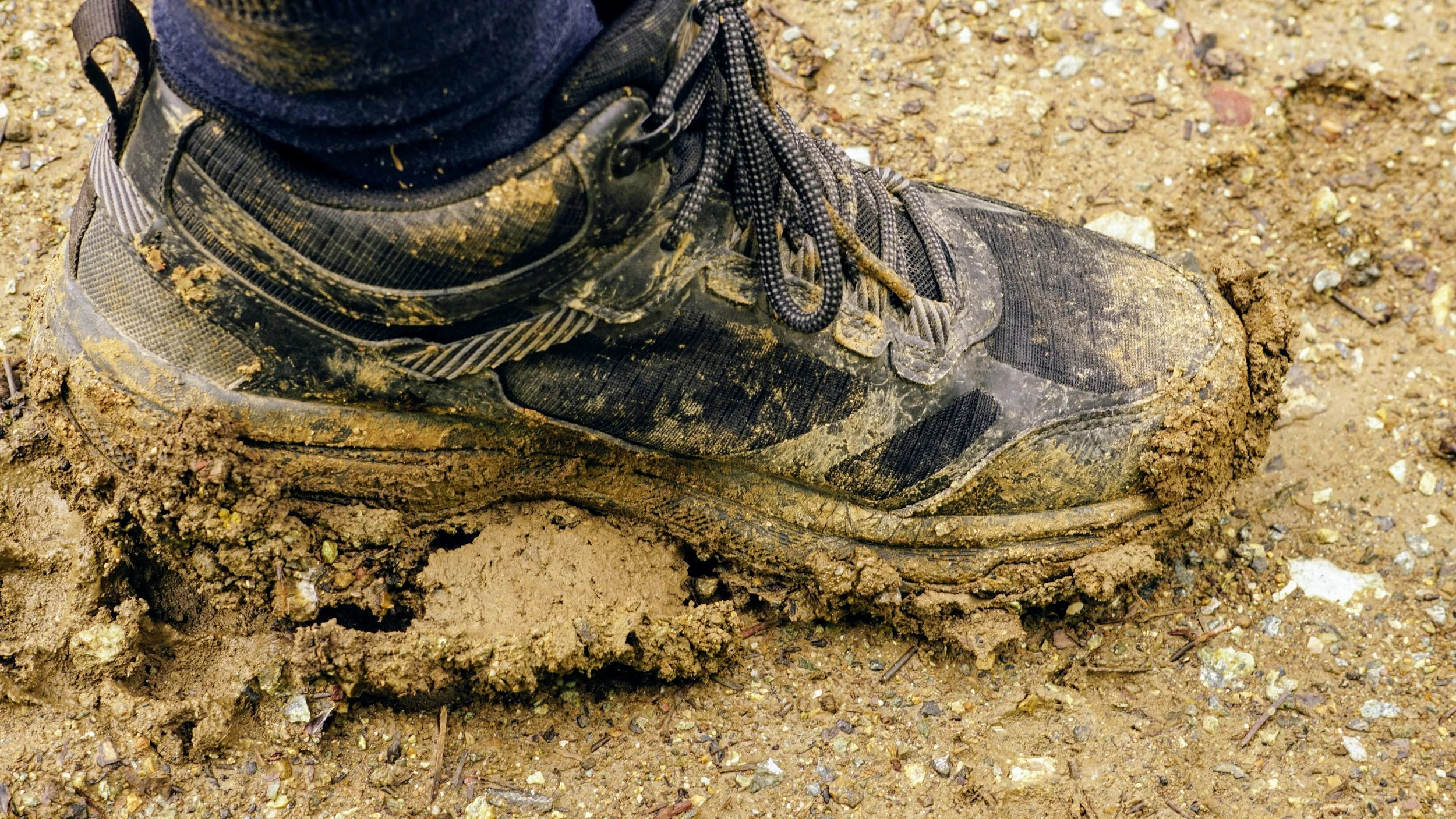 Close-up of a muddy hiking boot on a dirt trail.