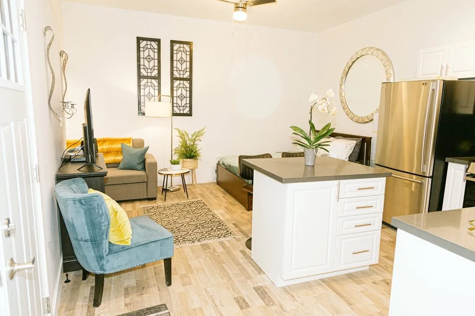 Living room and kitchen with furniture, plants, decorative wall art, and a refrigerator.