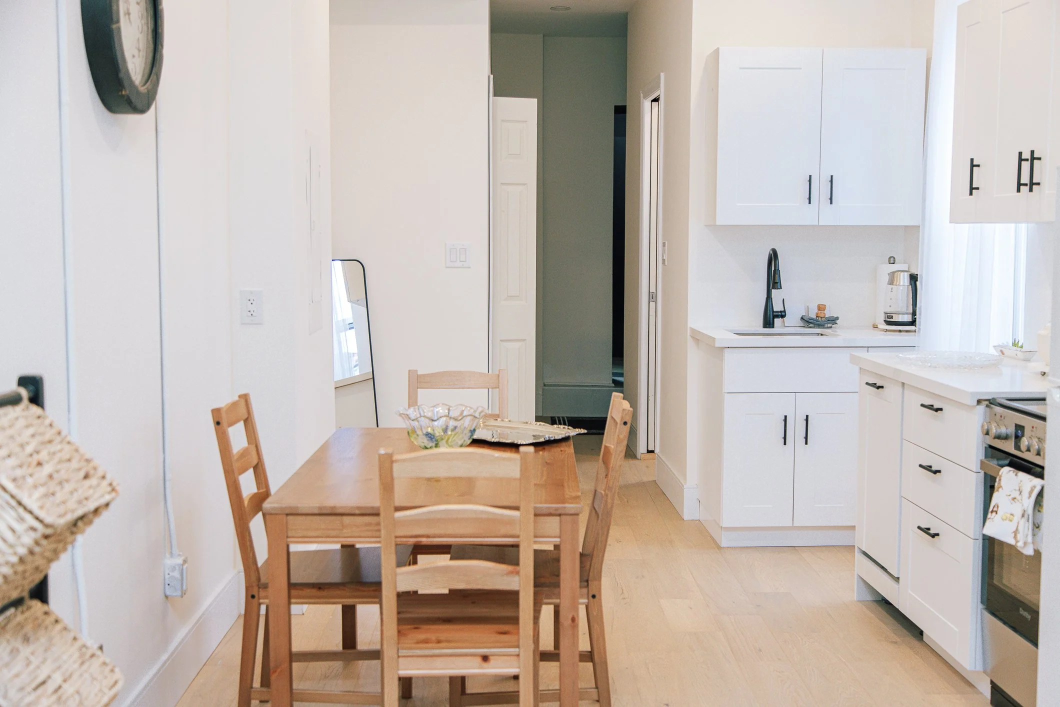 View of a kitchen and dining area with a wooden table and chairs, white cabinets, a sink with a black faucet, and a white stove in a bright, clean space.
