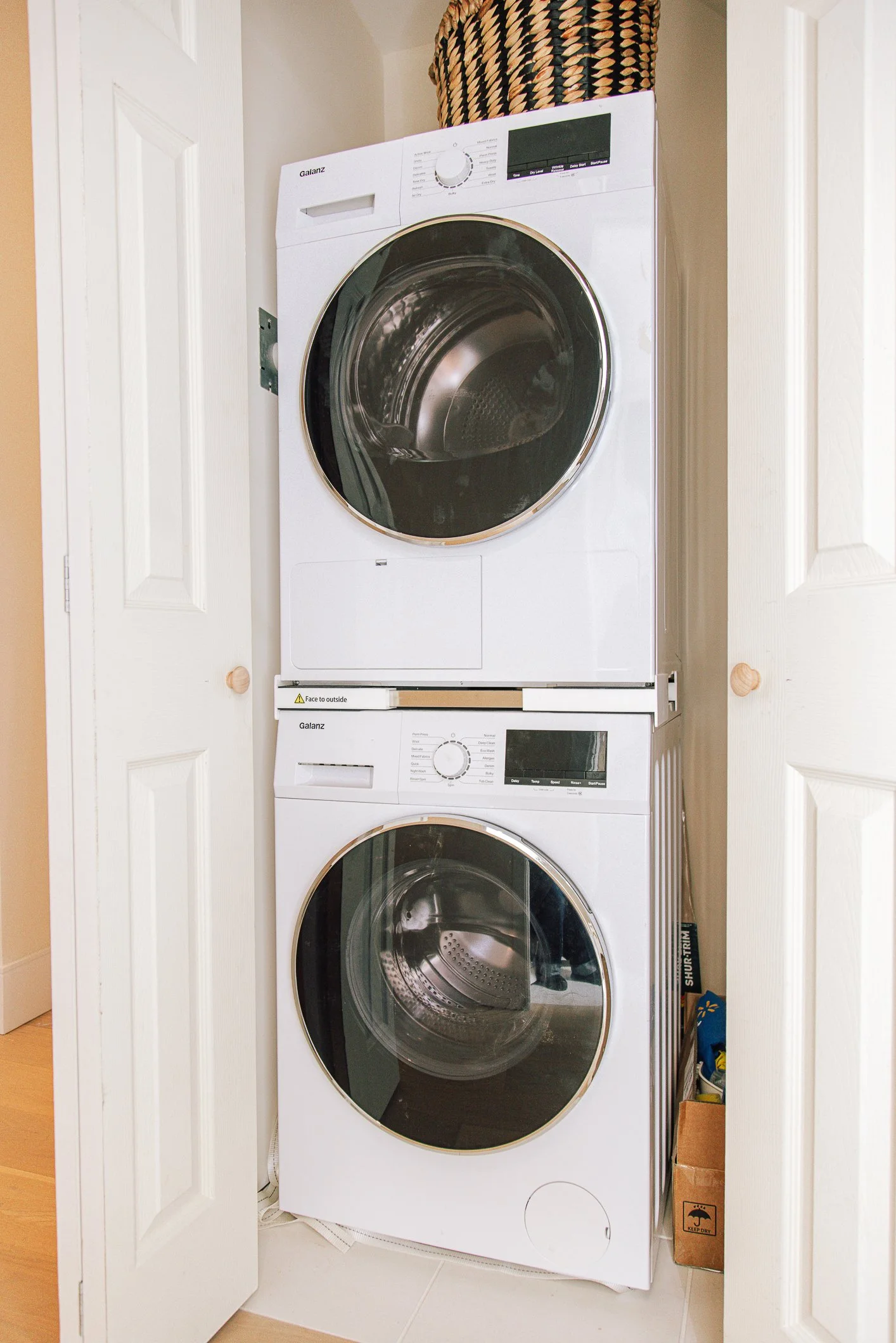 Stacked front-loading washing machine and dryer in a small laundry closet with white doors open.