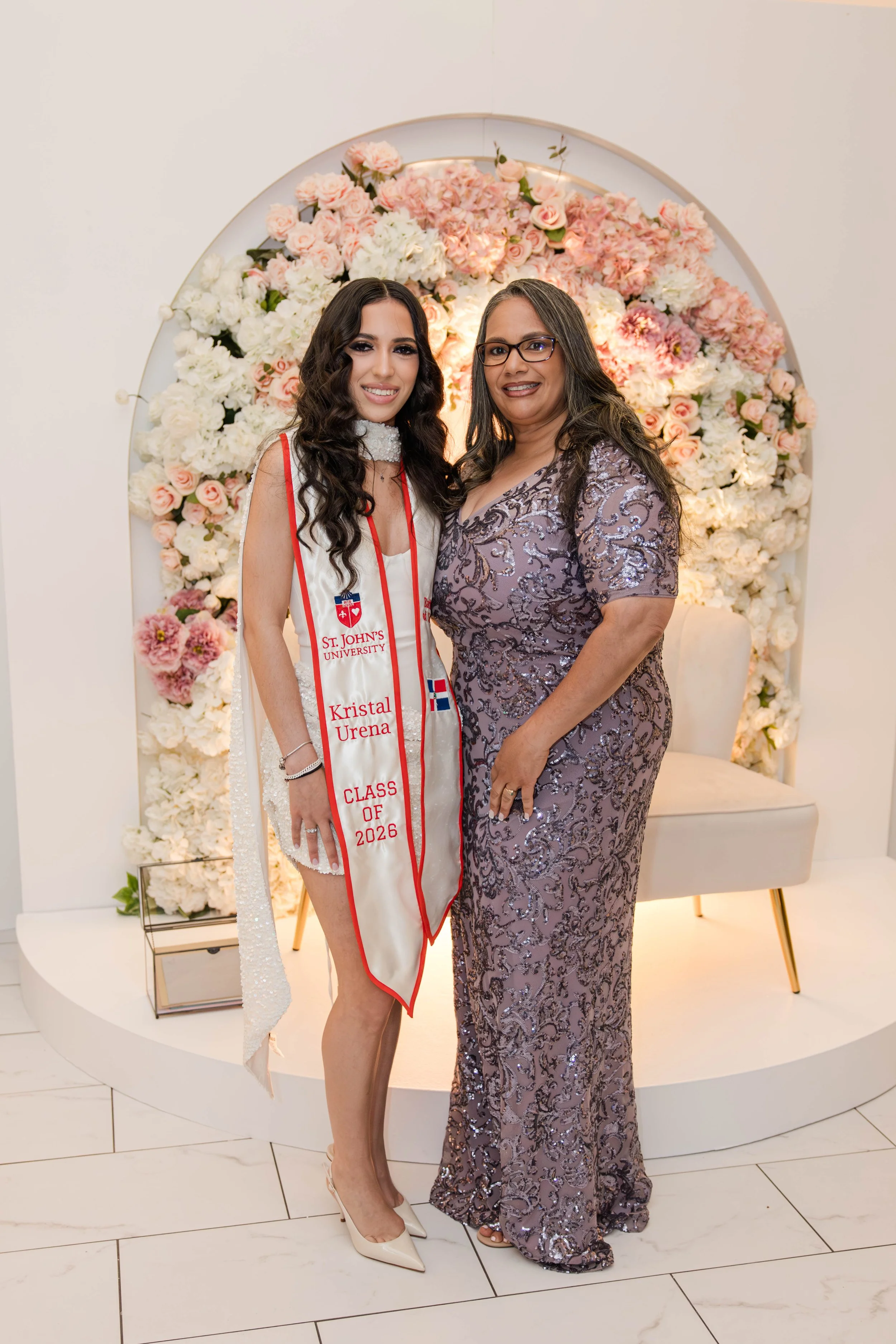 Mother and daughter graduation portrait in front of a soft pink and white floral backdrop in Freeport NY by Moon & Stars Photography.