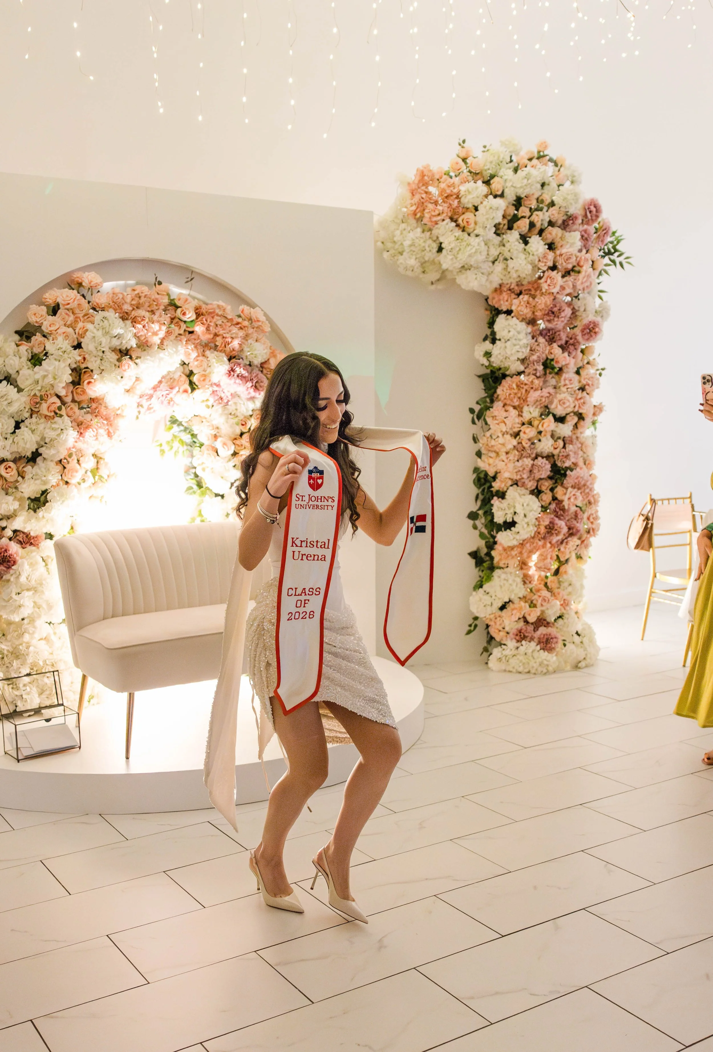St. John’s University graduate dancing with her graduation stole at a floral decorated celebration venue in Freeport NY. Photographed by Moon And Stars Photography