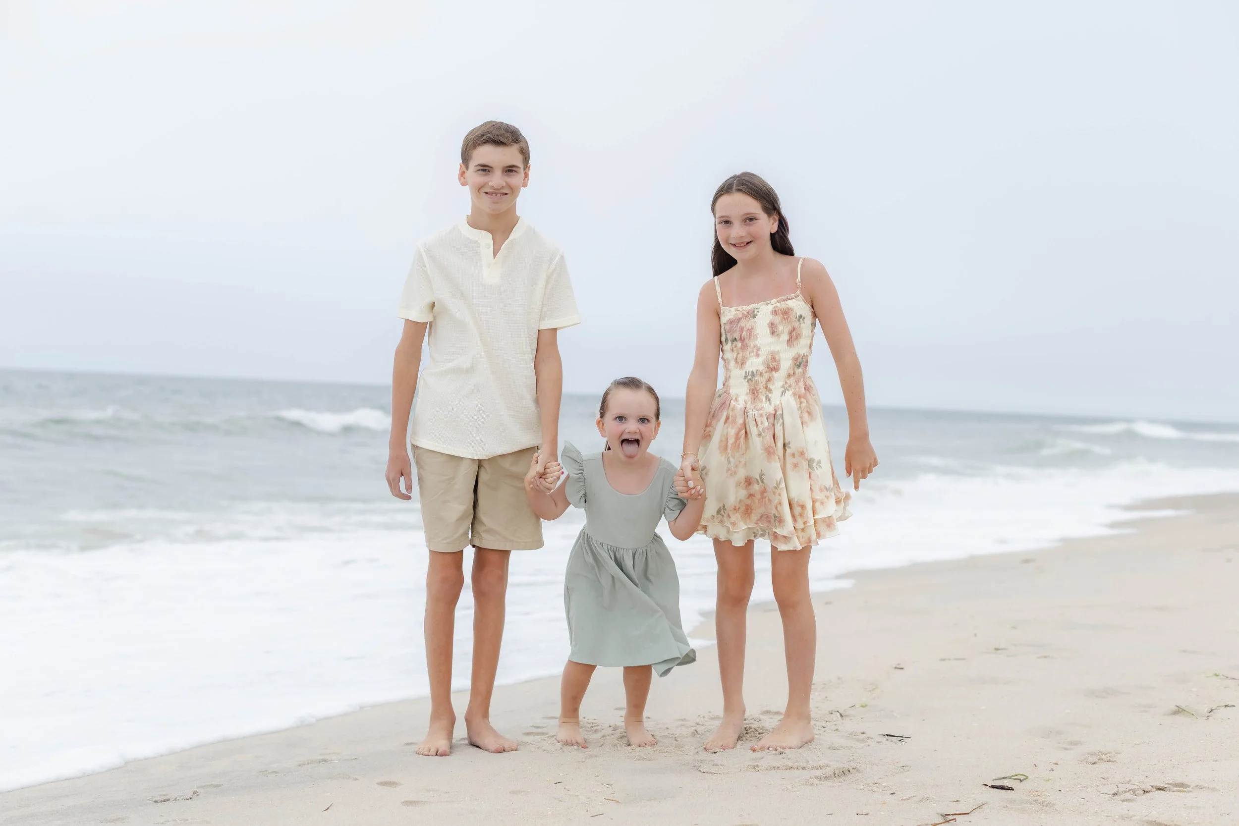 Playful sibling portrait on a Long Island beach with ocean waves in the background captured during a family photography session