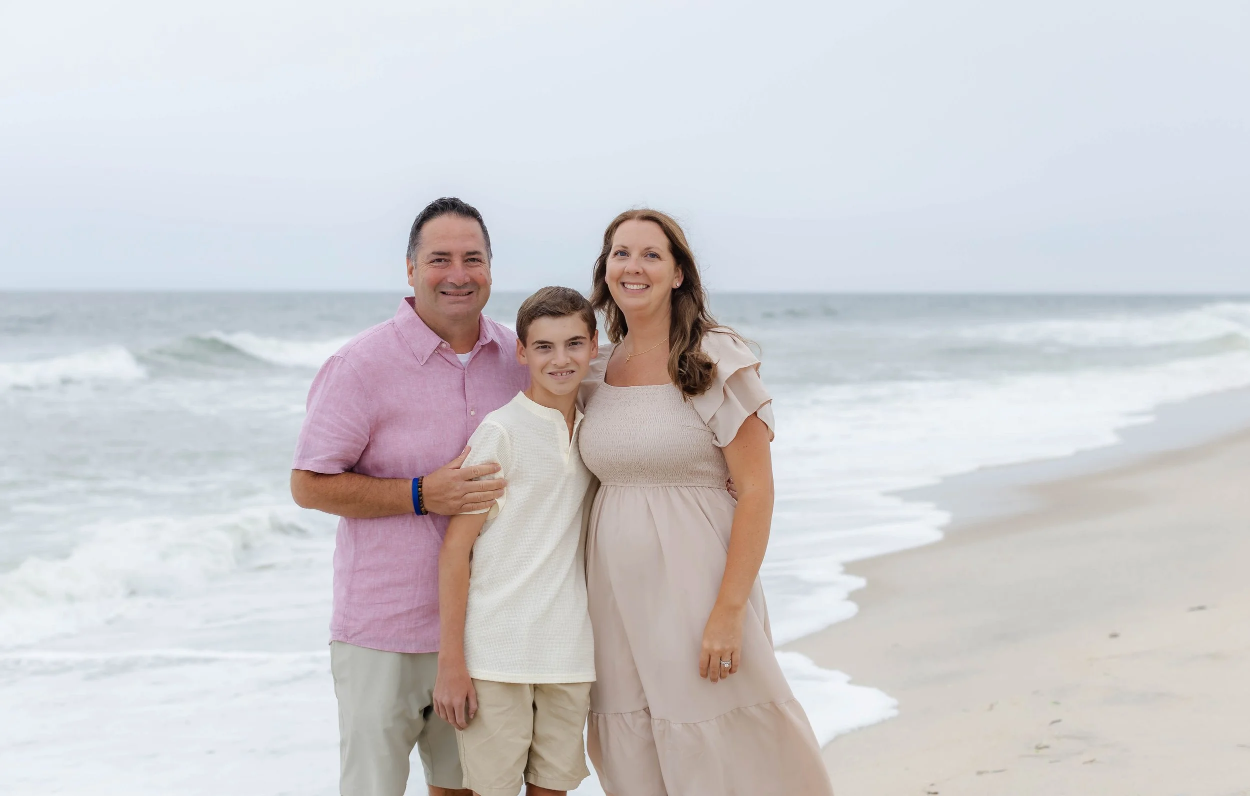 Family portrait on the shoreline of a Long Island beach with soft waves and natural light, captured in a light and airy photography style