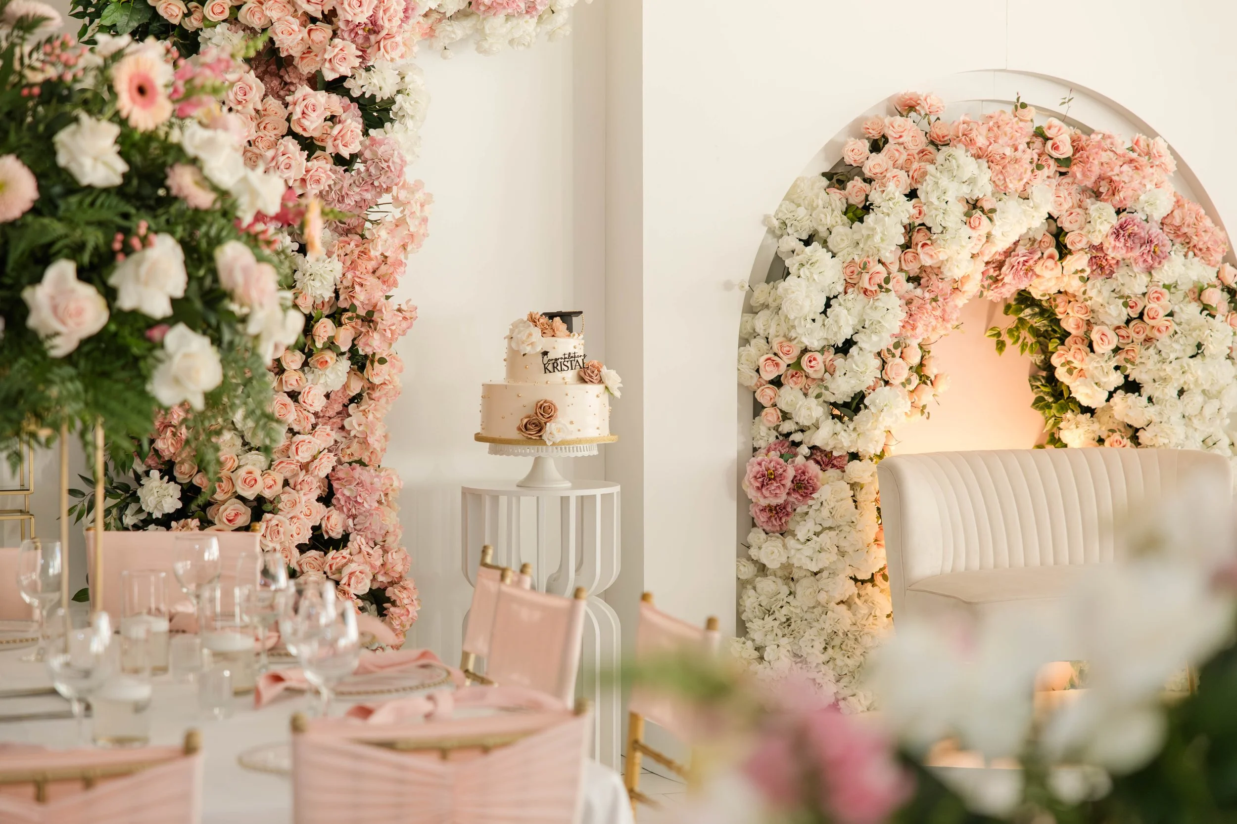 Elegant graduation party décor with pink florals, white seating, cake display, and soft event lighting at Margarets Venue Freeport NY.