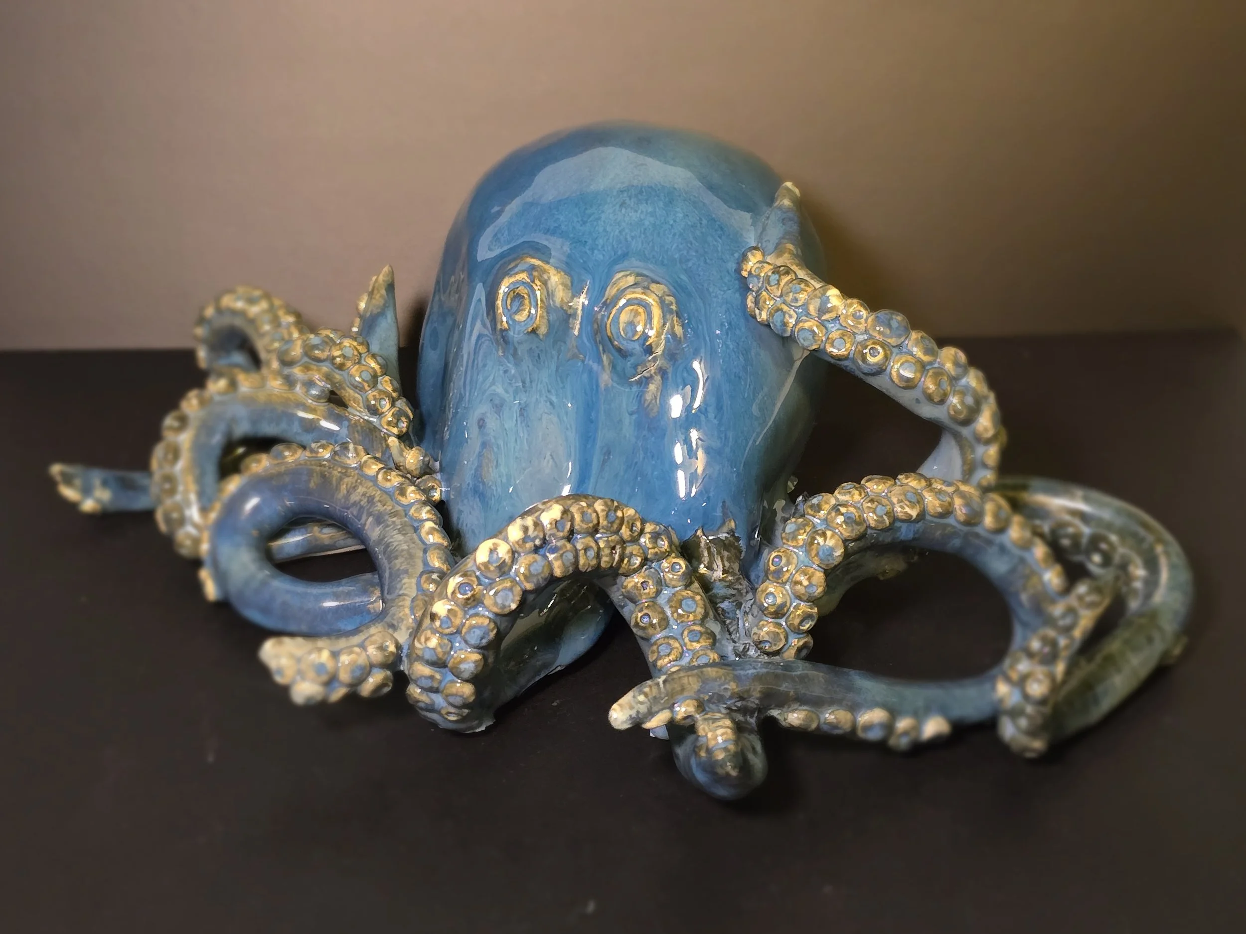 Blue ceramic octopus figurine with gold accents on tentacles, placed on a black surface.