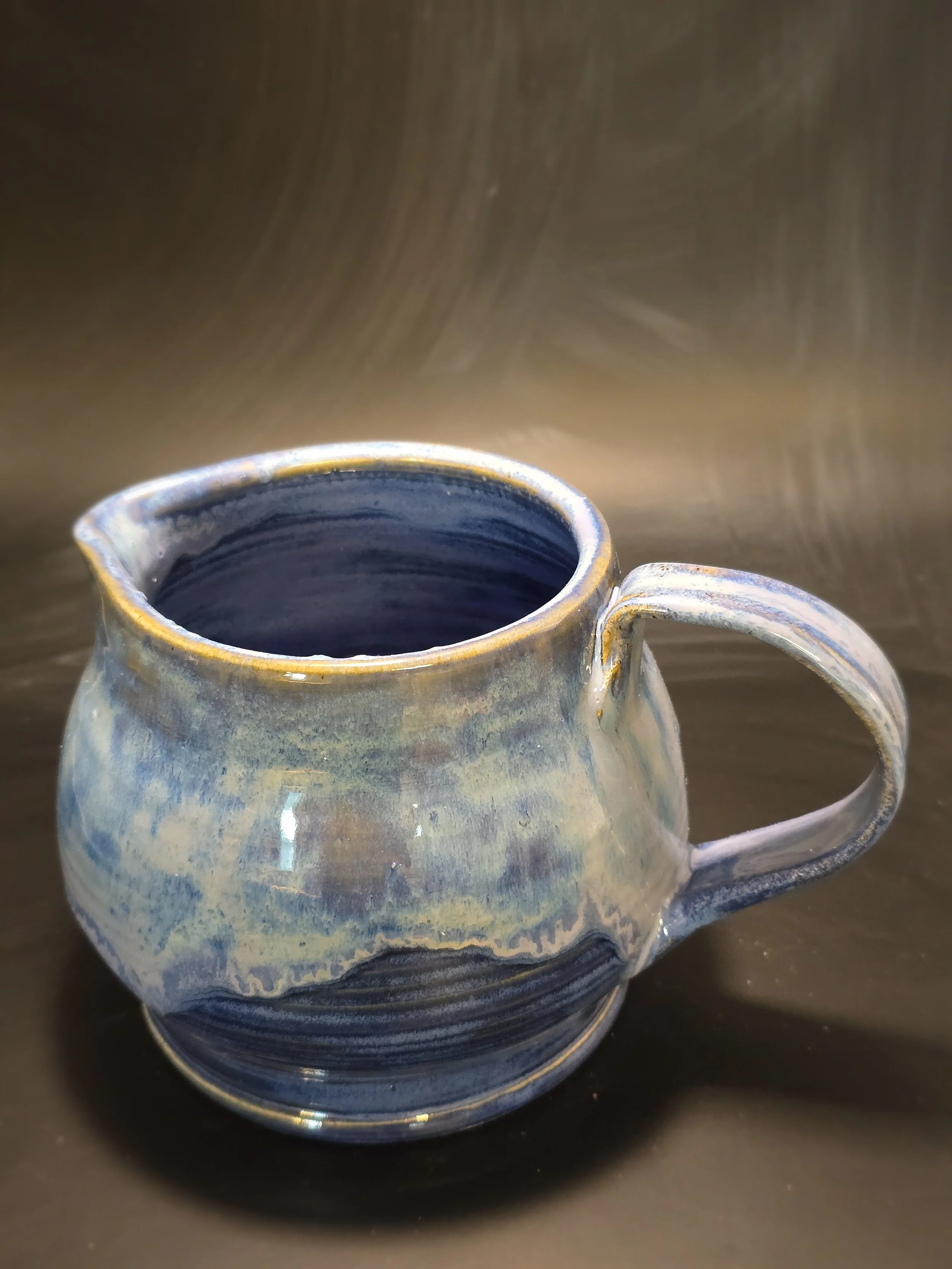 Close-up of a ceramic mug with a blue and beige glaze, placed on a black surface.
