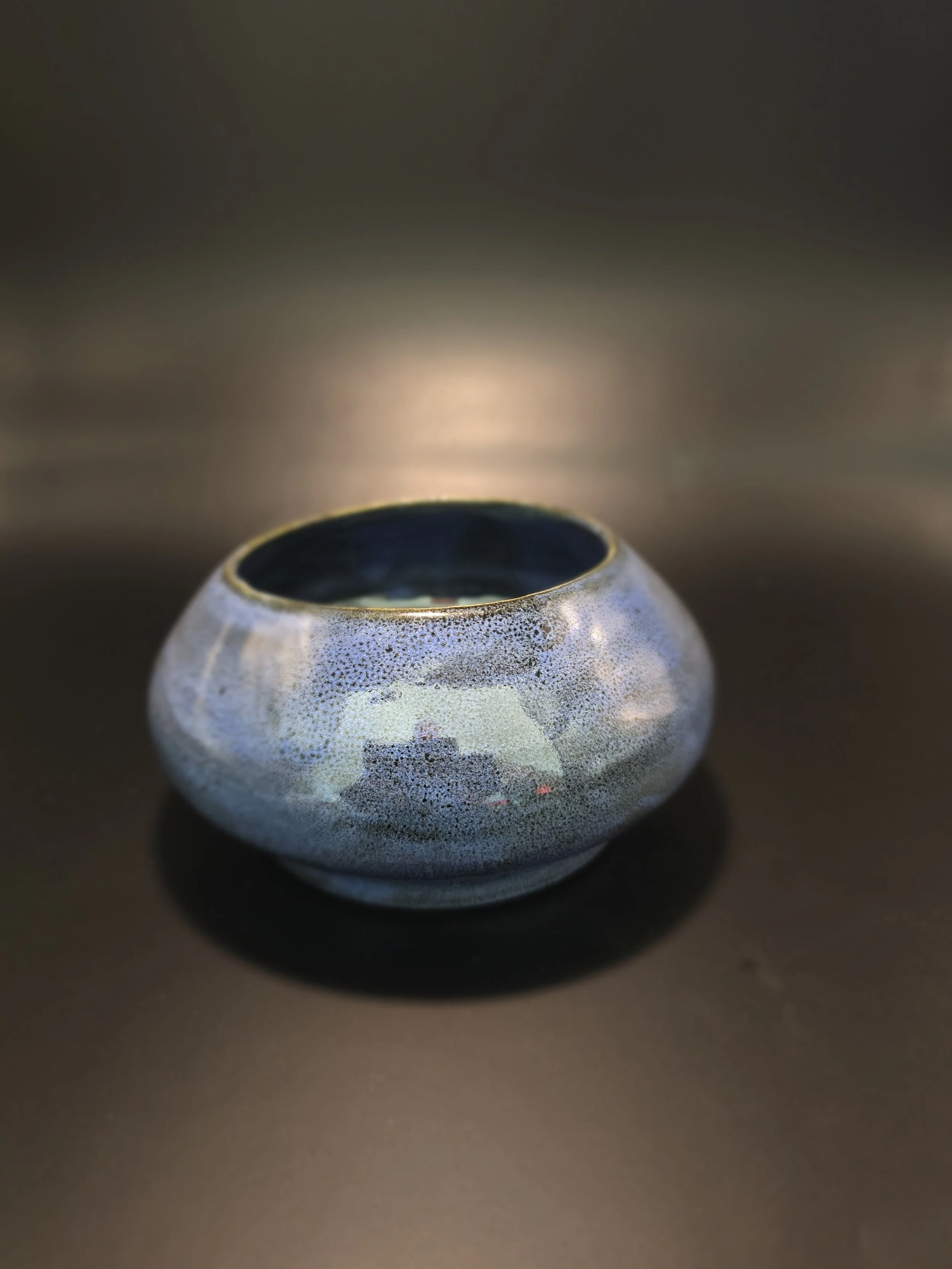 Ceramic bowl with a speckled glaze, dark interior, placed on a dark surface with a blurred background.