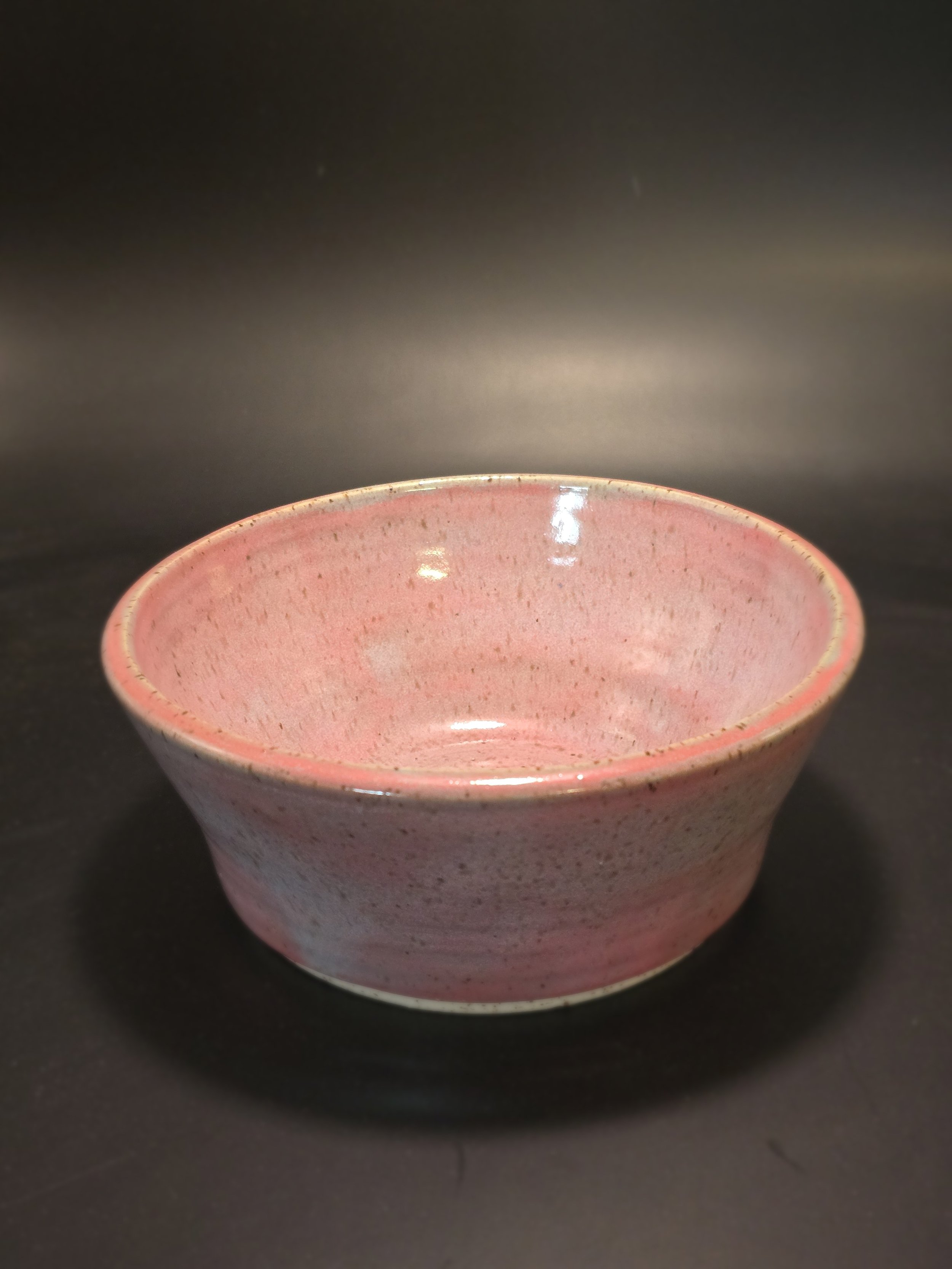 Pink ceramic bowl with a speckled pattern on a black surface.