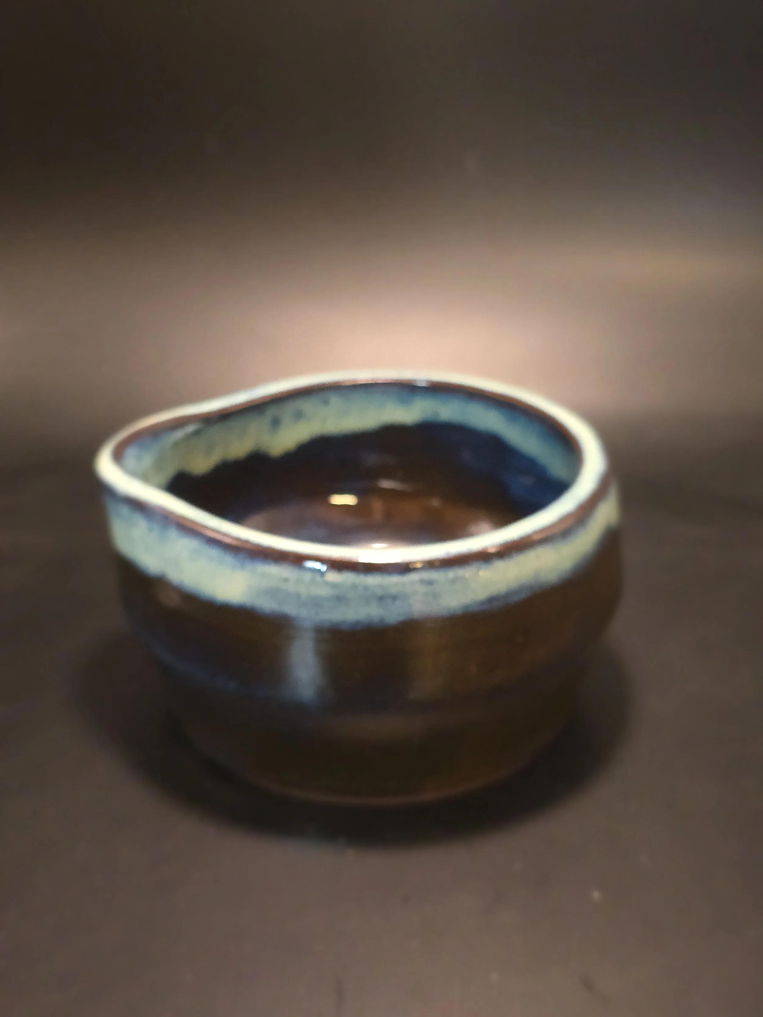 Brown ceramic bowl with a glazed top rim, sitting on a dark surface, with a blurred gradient background.