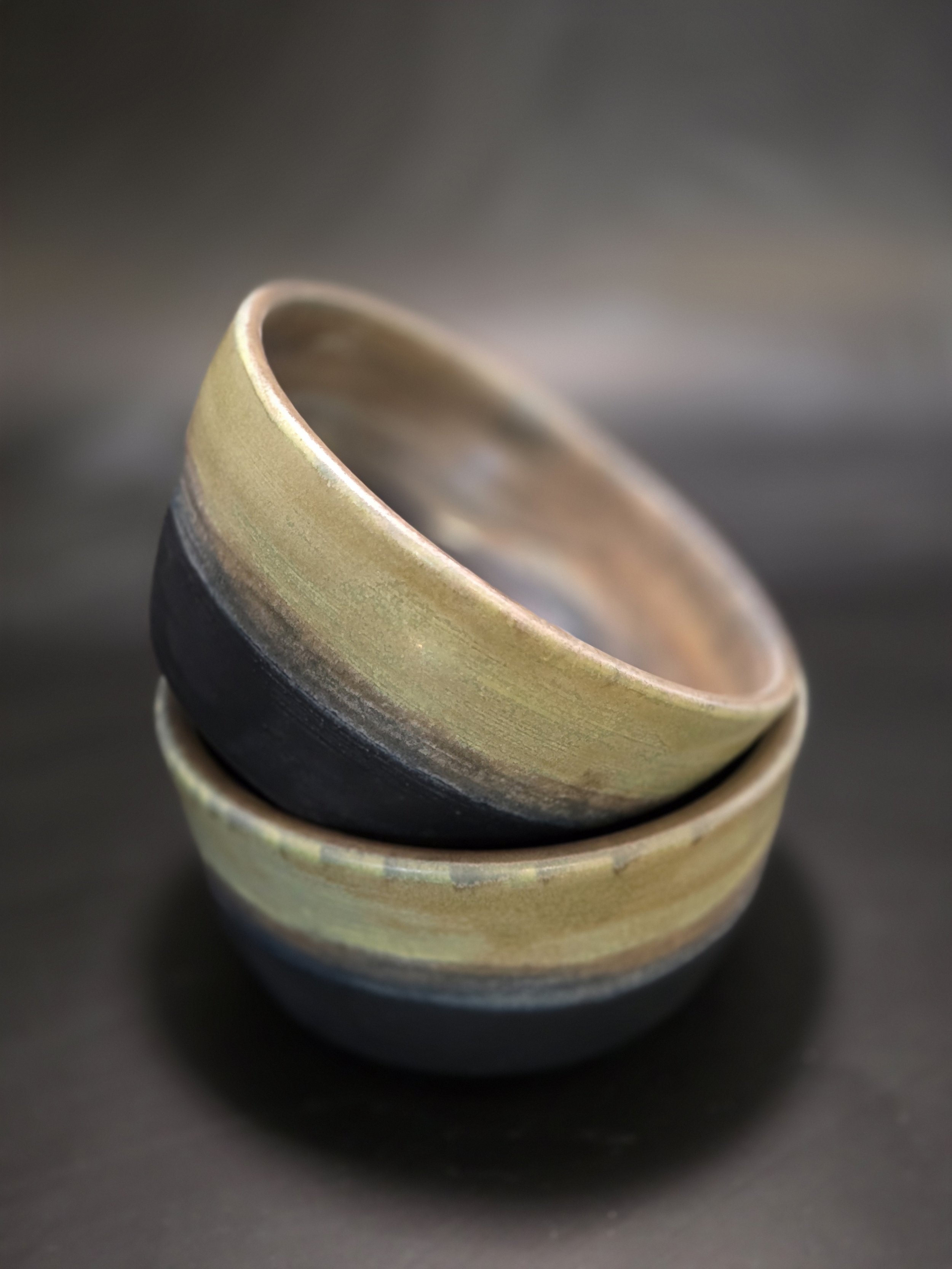 Stacked ceramic bowls with a glossy finish, dark outer surface, and beige interior, placed on a black background.