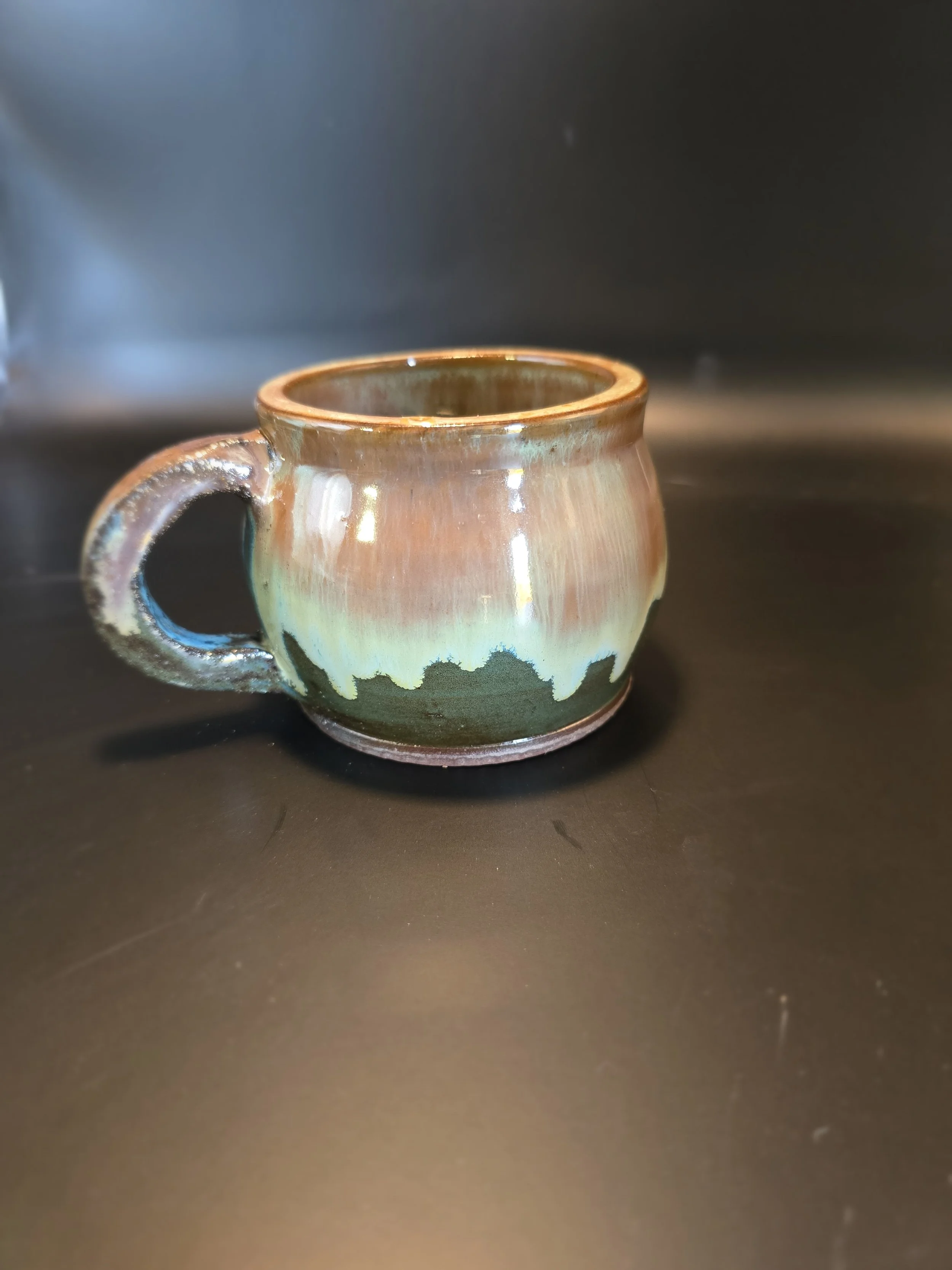 A small ceramic mug with a glazed, colorful design featuring earthy tones and abstract patterns