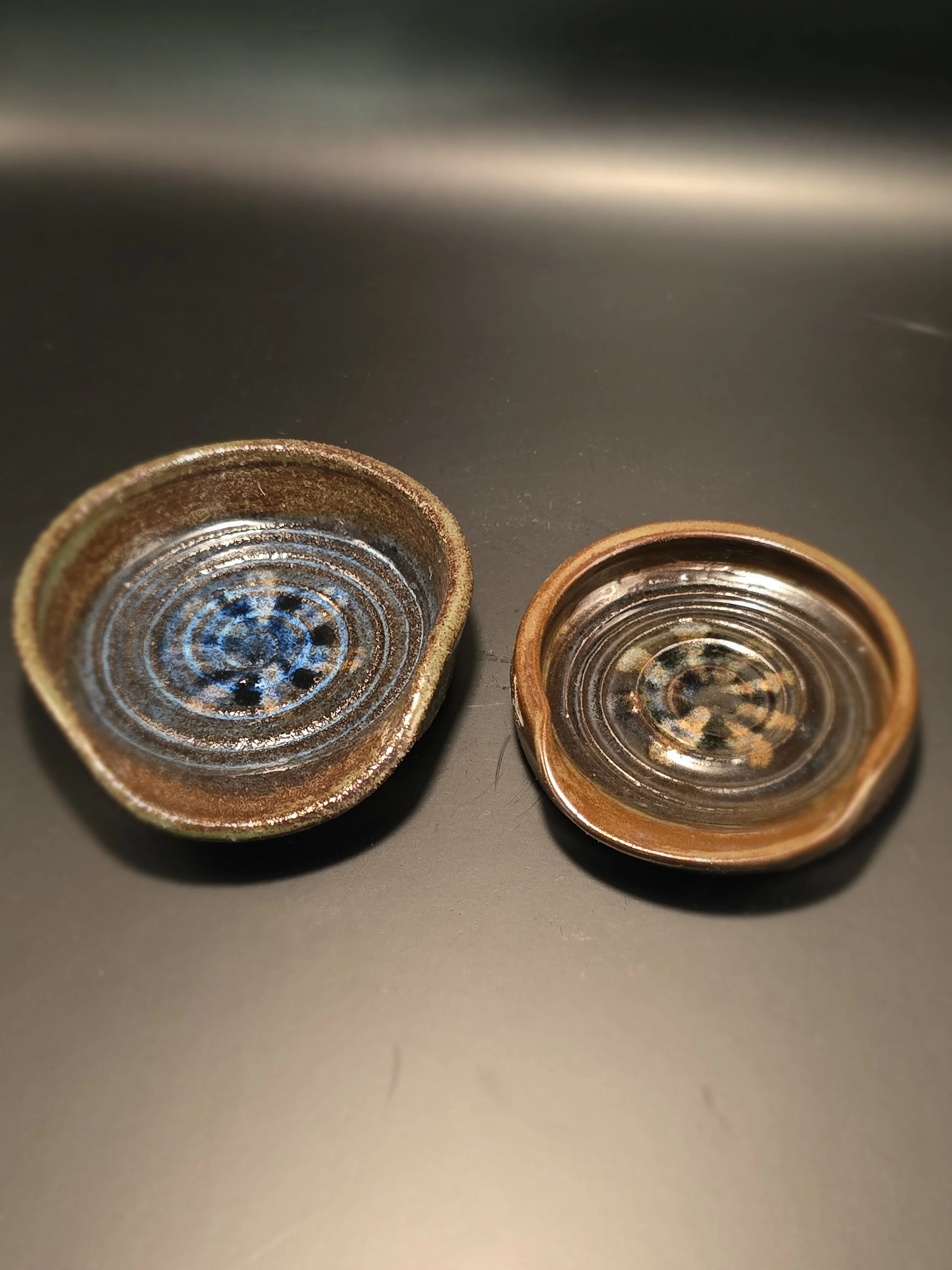 Two small ceramic or pottery dishes with spiral patterns and glazed interiors, placed on a dark surface.