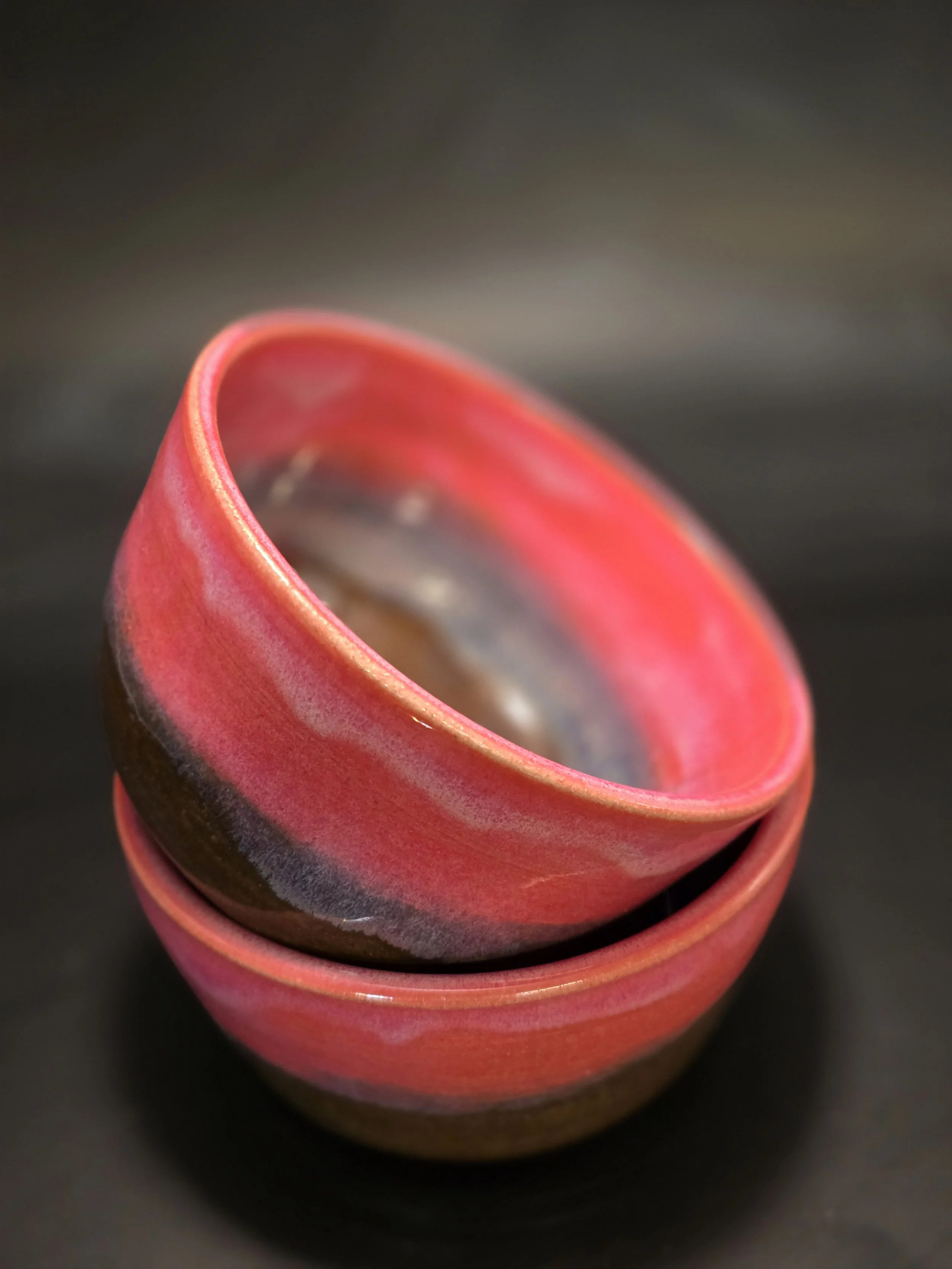 Close-up of a red and pink layered ceramic cup against a dark background.