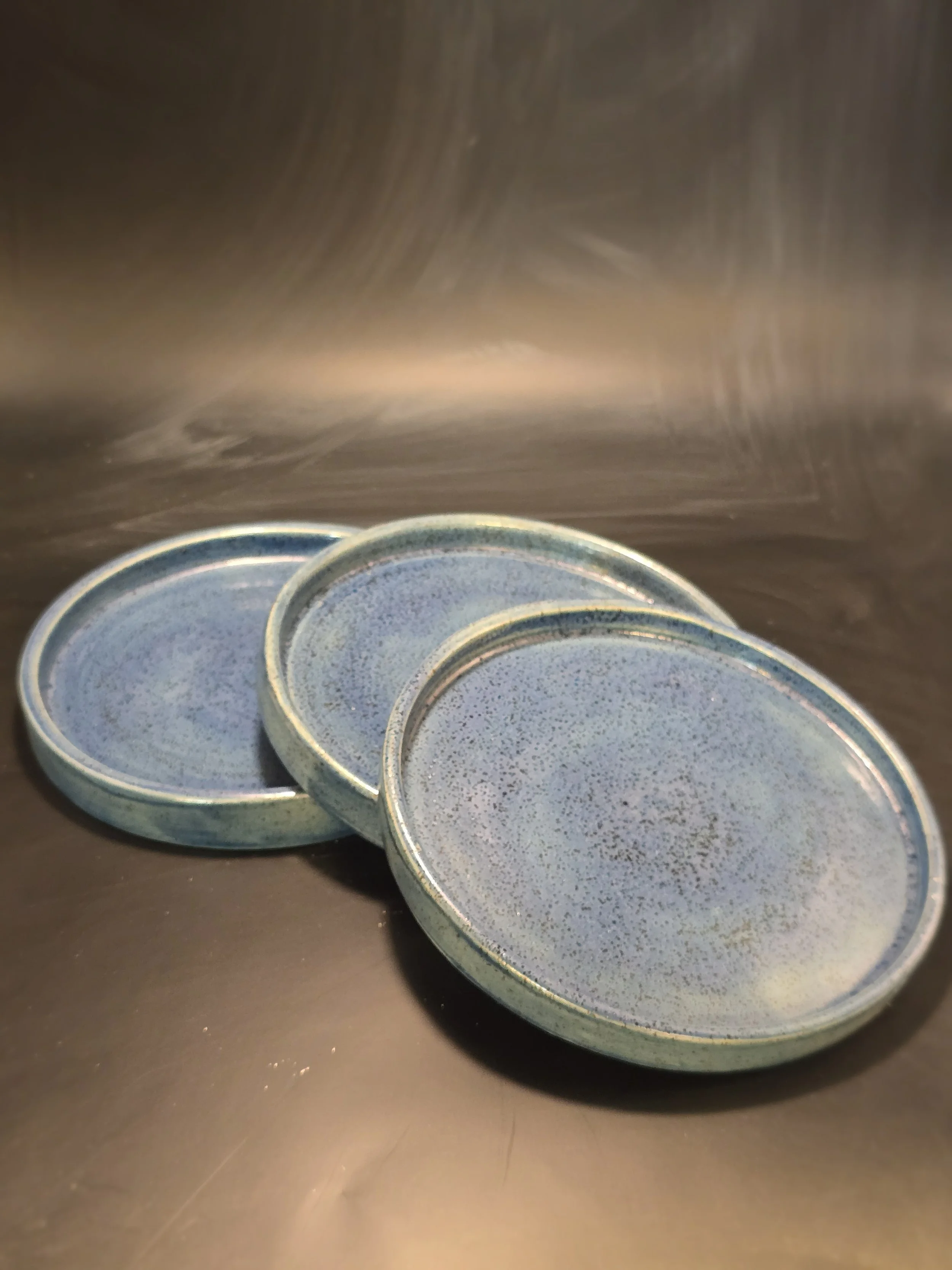 Three ceramic bowls with a speckled blue and green glaze placed on a dark surface.