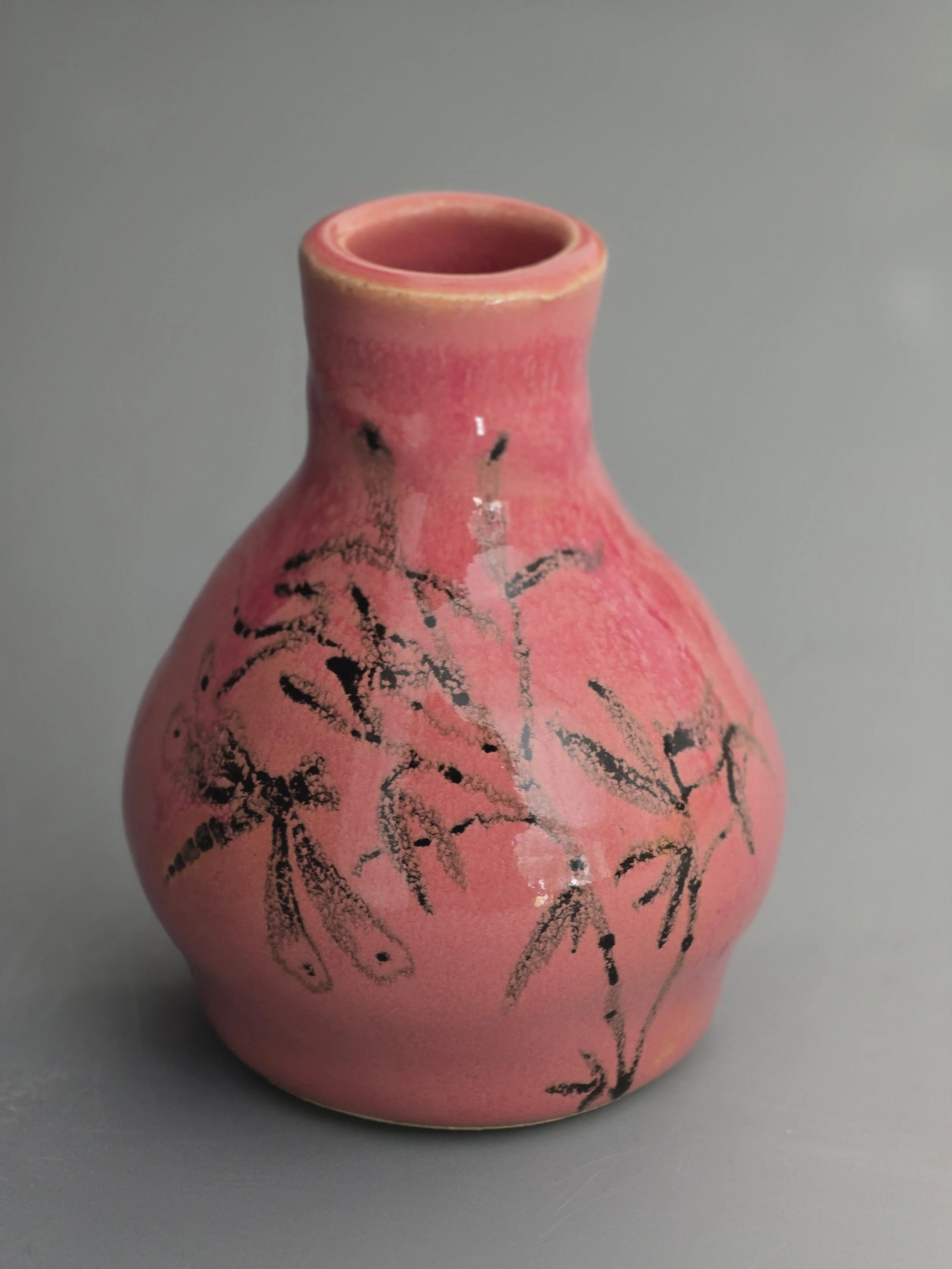 Pink ceramic vase with black leaf and branch designs on a gray background.