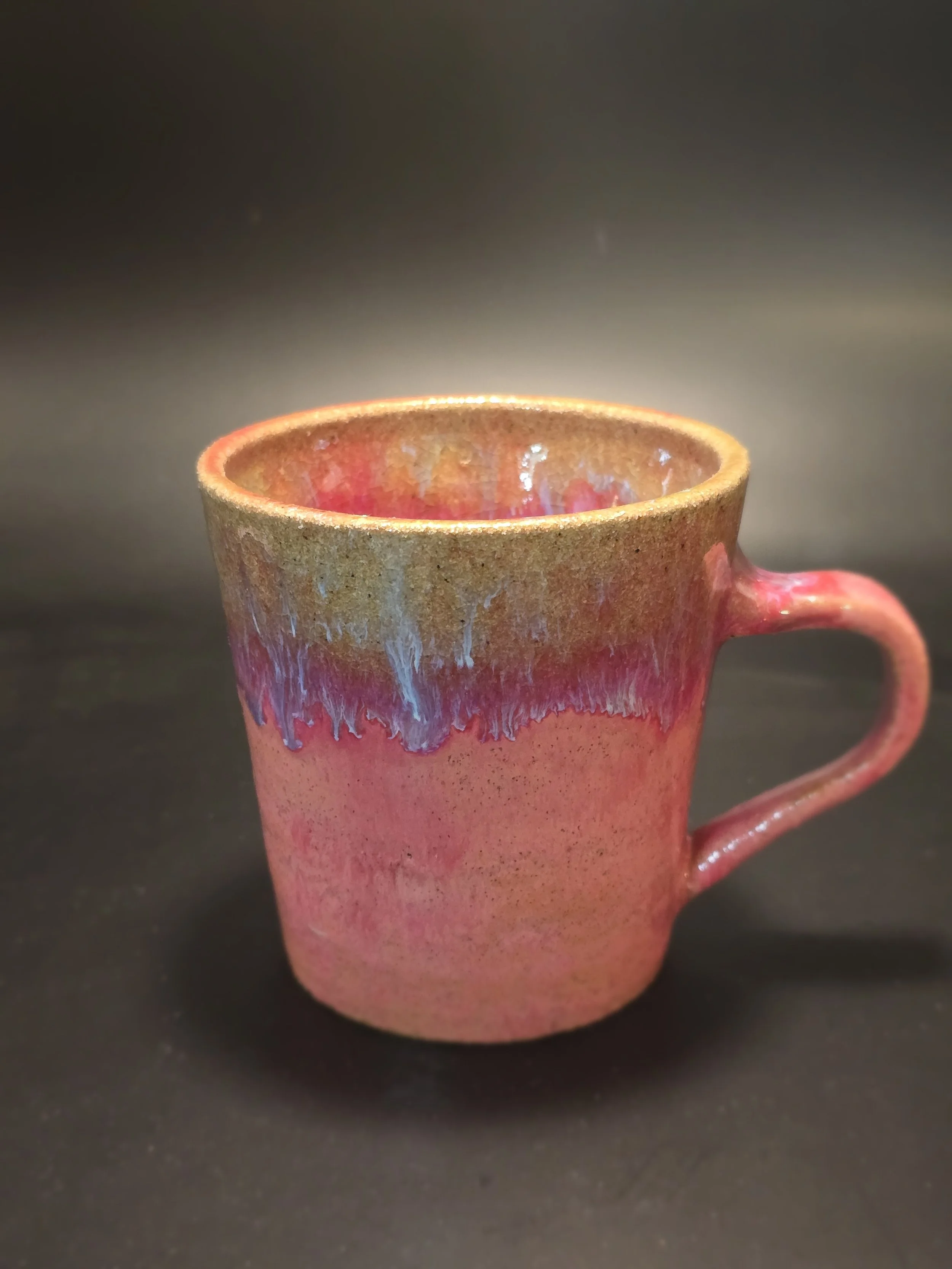 A ceramic mug with a pink and brown glaze, placed on a black surface.