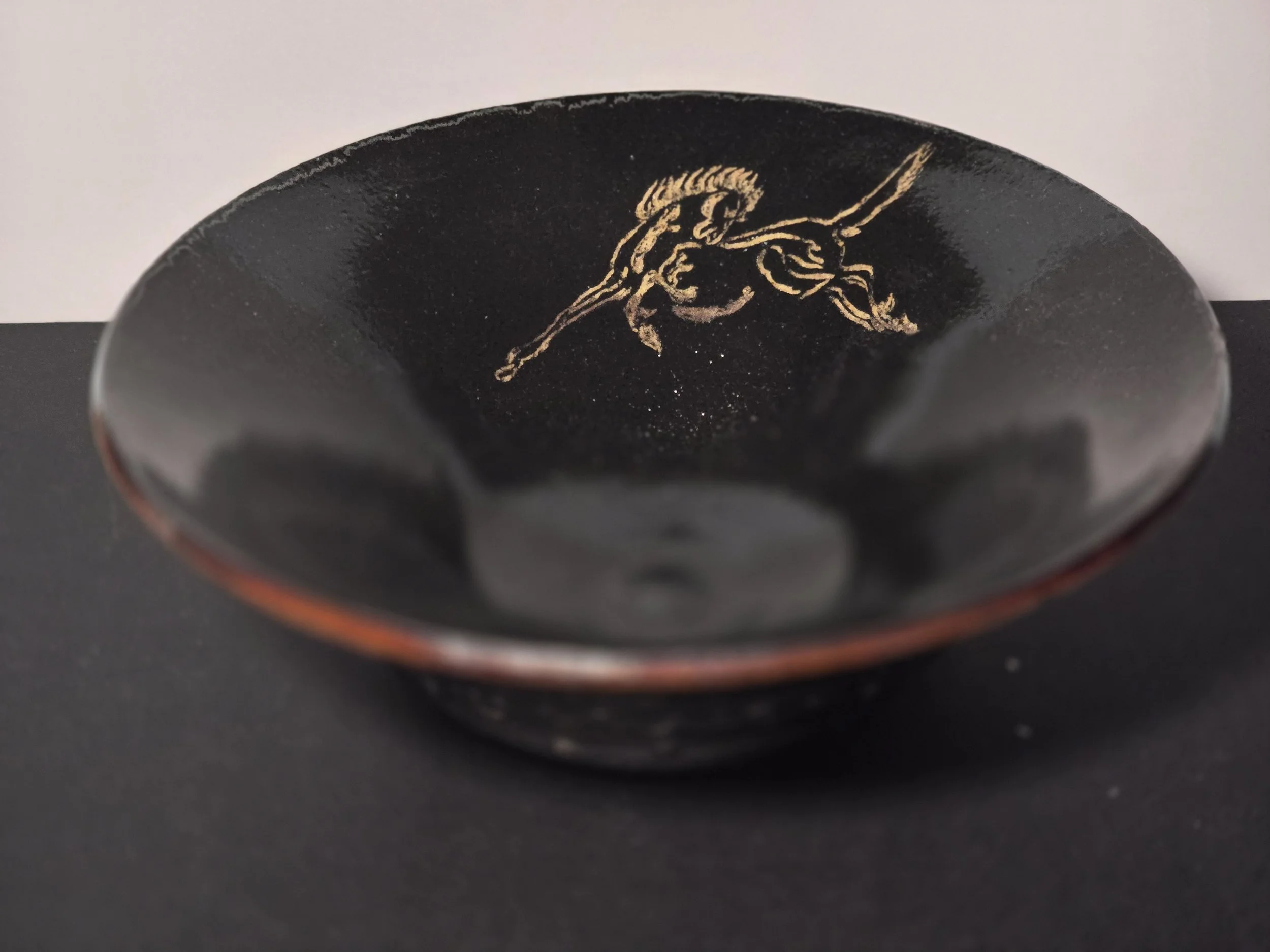 Black ceramic bowl with gold illustration of a warrior on horseback inside.
