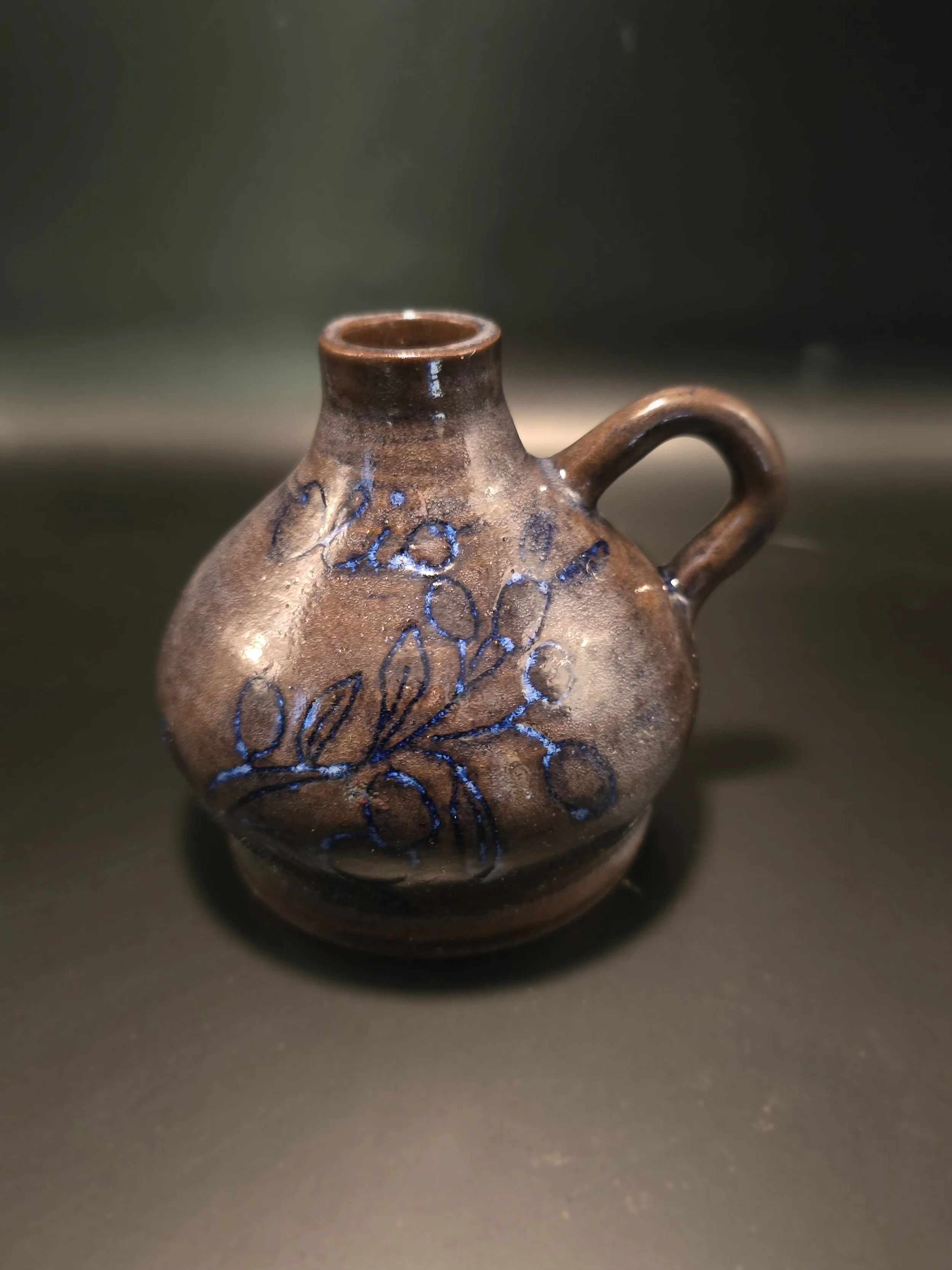 Small ceramic jug with a handle, decorated with blue floral or leaf patterns and words written in blue.