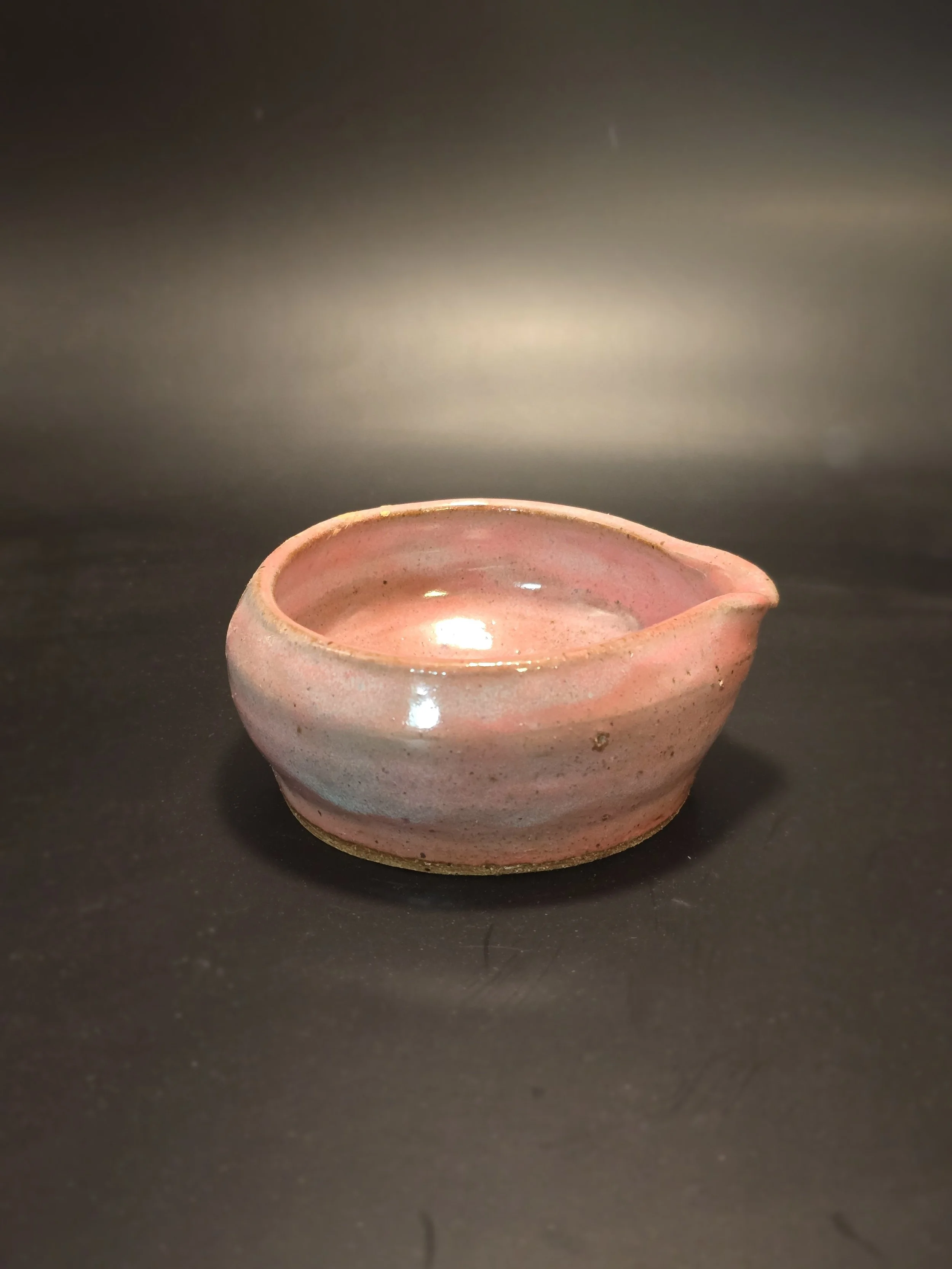 Small pink ceramic bowl on black surface with dark background.