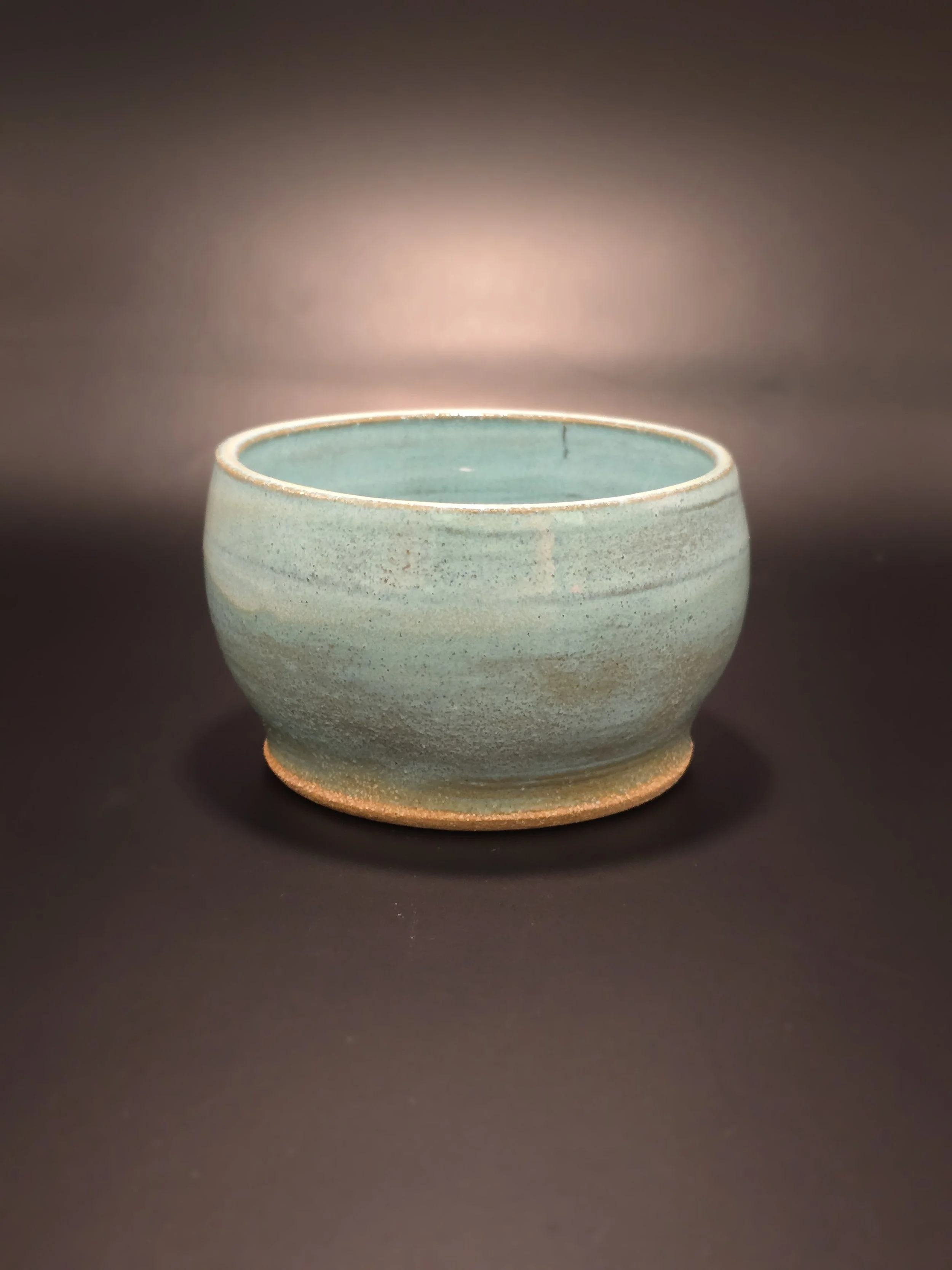 A ceramic bowl with a greenish glaze, placed against a dark background.