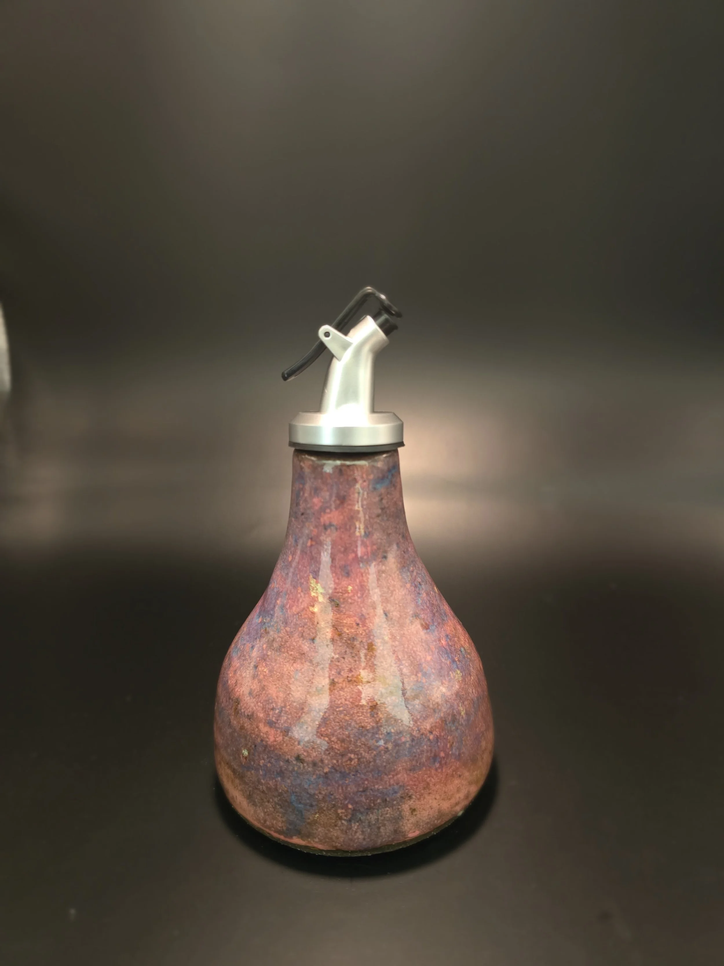 A textured vase with a rust-like finish and a silver spout attached to a black lid.