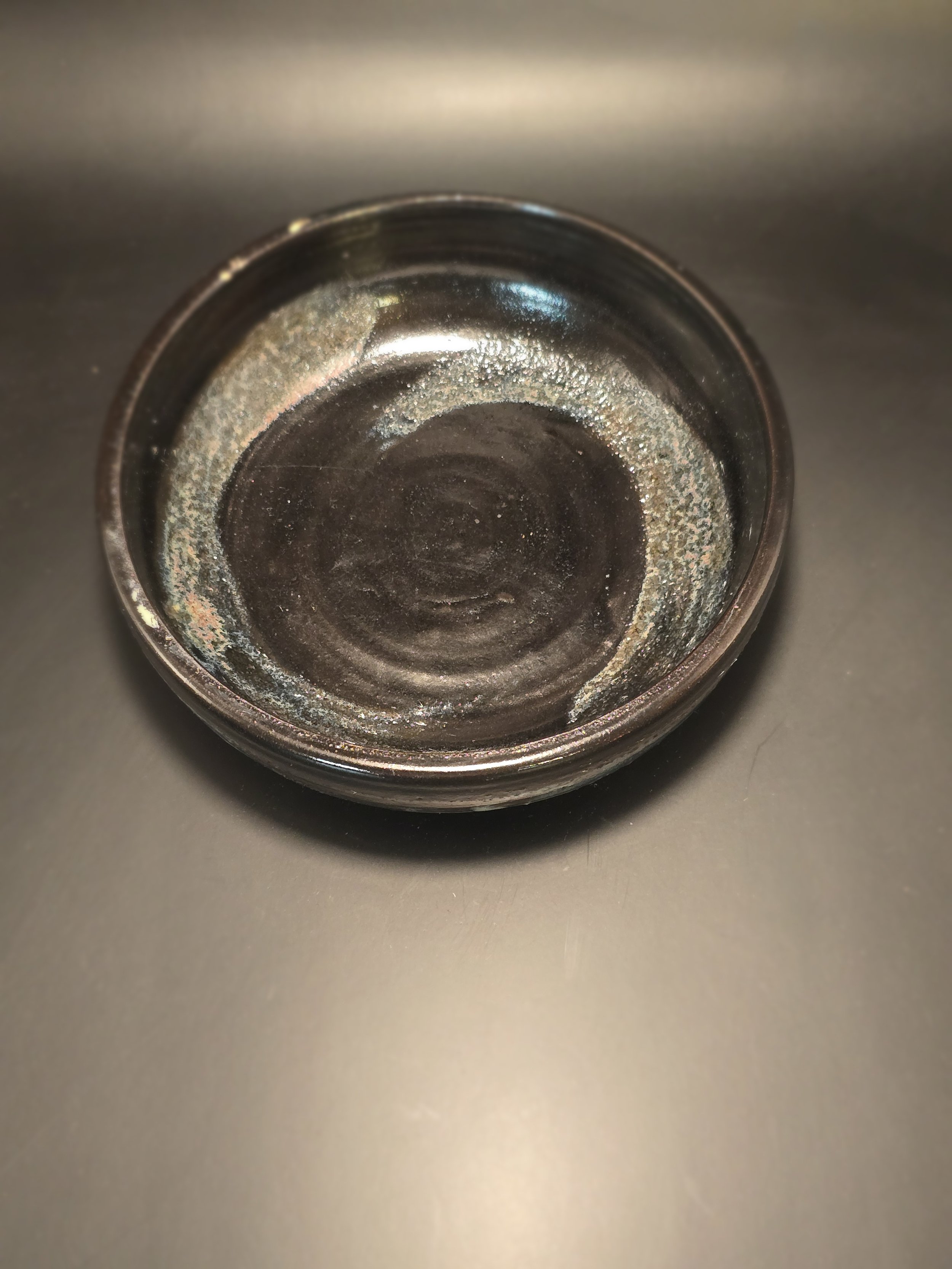 Empty black ceramic bowl with some residue and discoloration inside, placed on a gray surface.