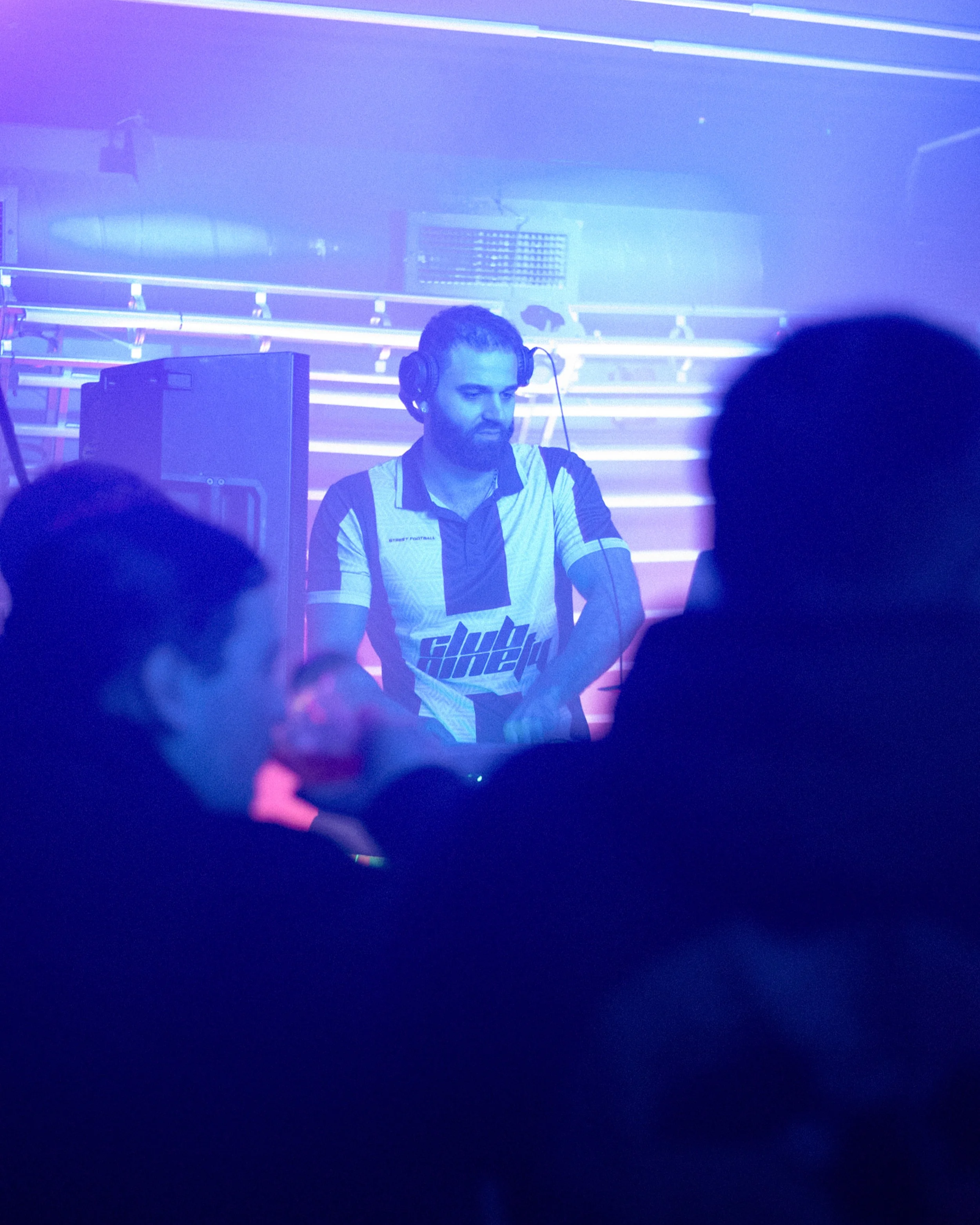 A DJ with headphones working at a turntable in a club with purple and blue lighting effects.
