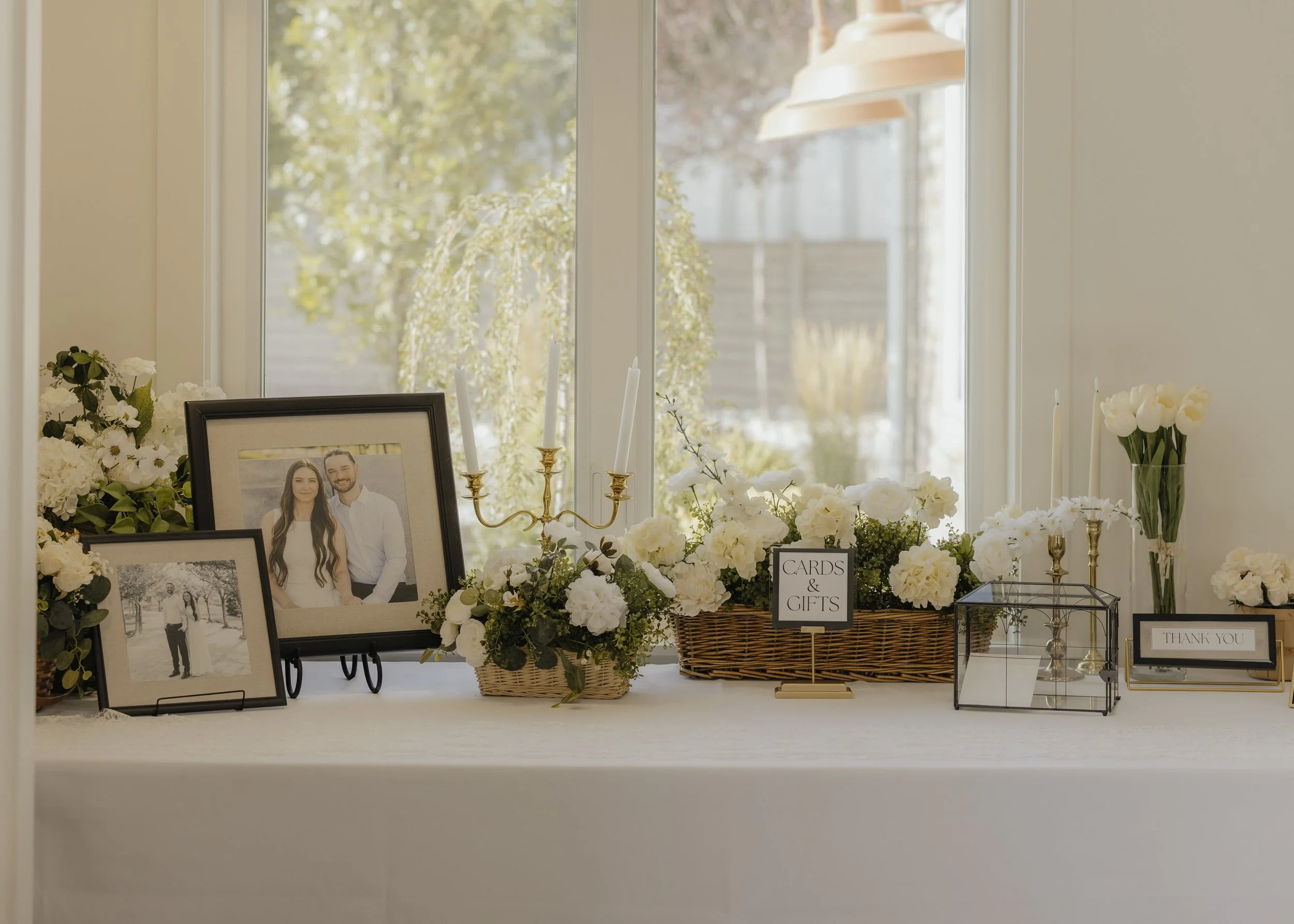 A table decorated with framed photos of a couple, white flowers, candles, and signs that say 'Cards & Gifts' and 'Thank You'.