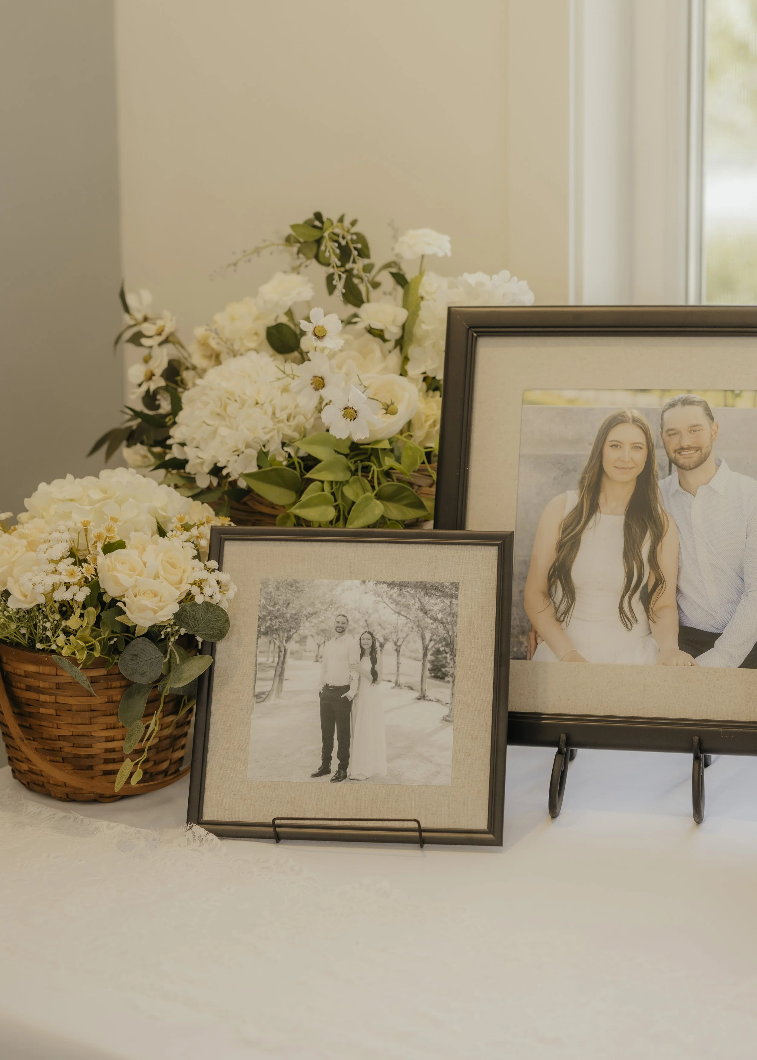 Wedding photographs and floral arrangements on display, including framed pictures of a happy couple and a black-and-white photo of the same couple, with white and green flowers in baskets.