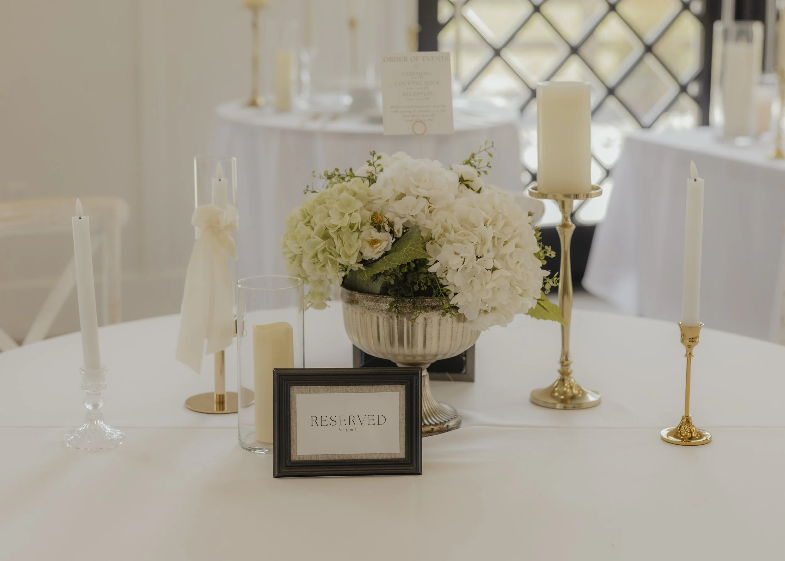 A decorated table with white flowers, candles, and a reserved sign for a wedding or event.