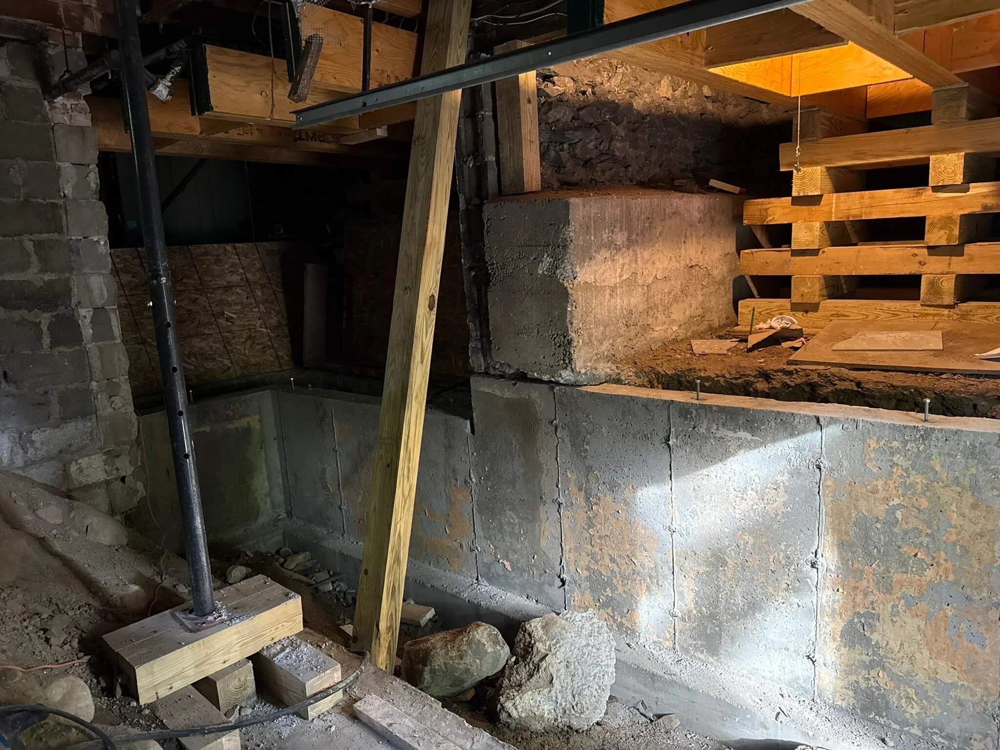 New concrete beneath old stone. Shoring keeps the house steady while the foundation is underpinned below.
