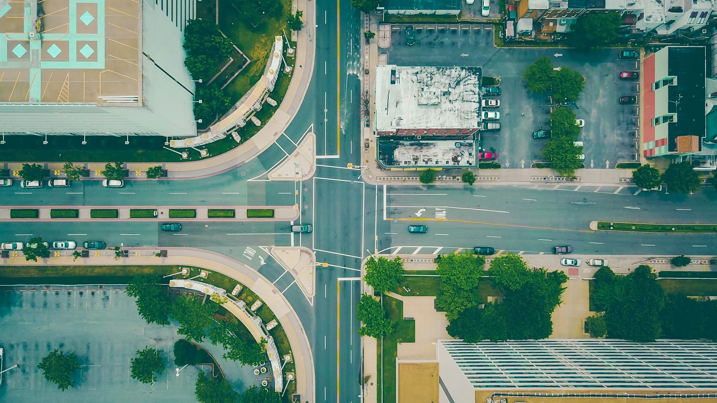 Vue aérienne d'une intersection urbaine avec des rues, des voitures, des bâtiments et des espaces verts.