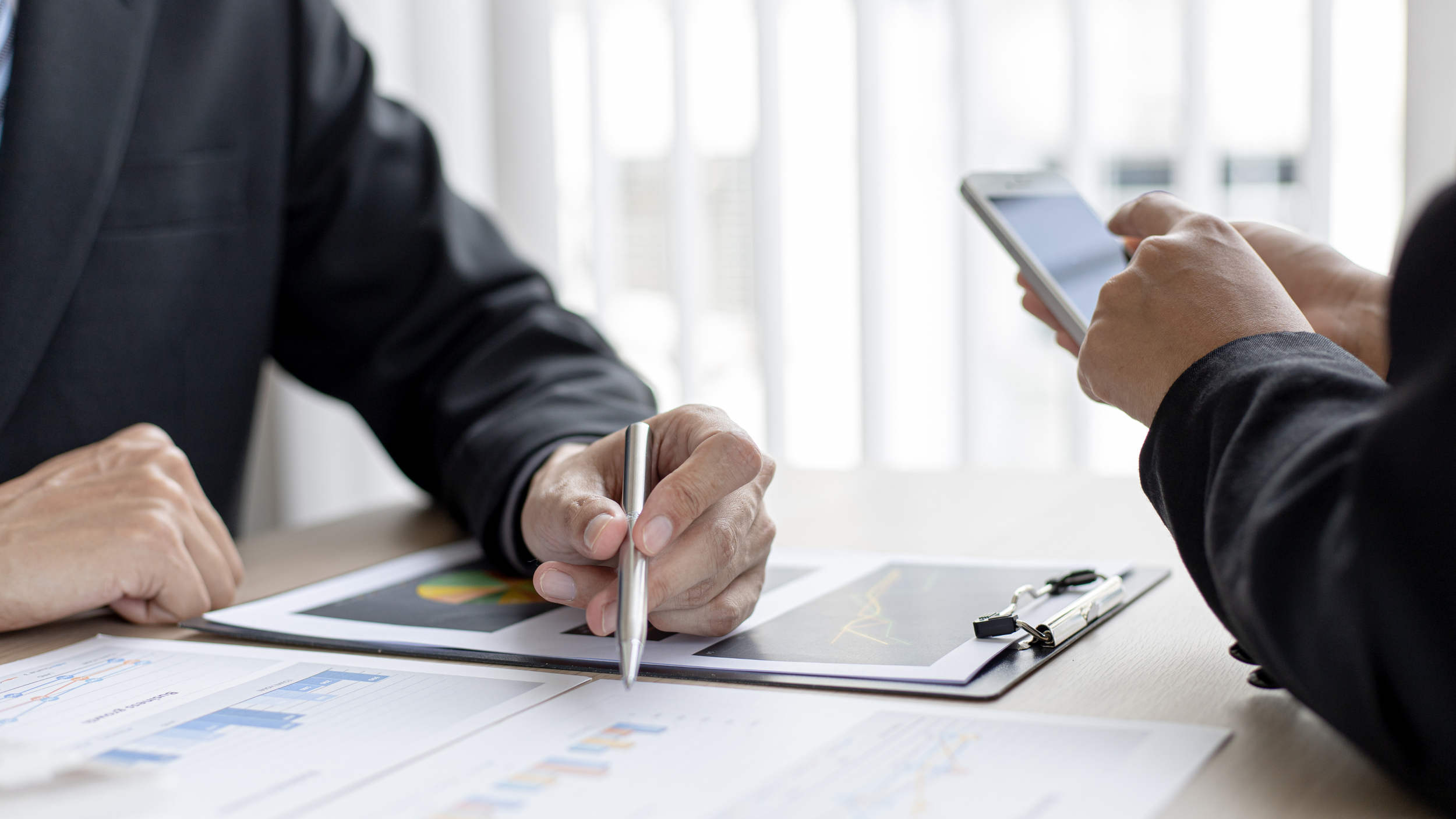 Deux personnes travaillent sur des documents avec des graphiques et des écrans de smartphones sur une table, dans un environnement de bureau.