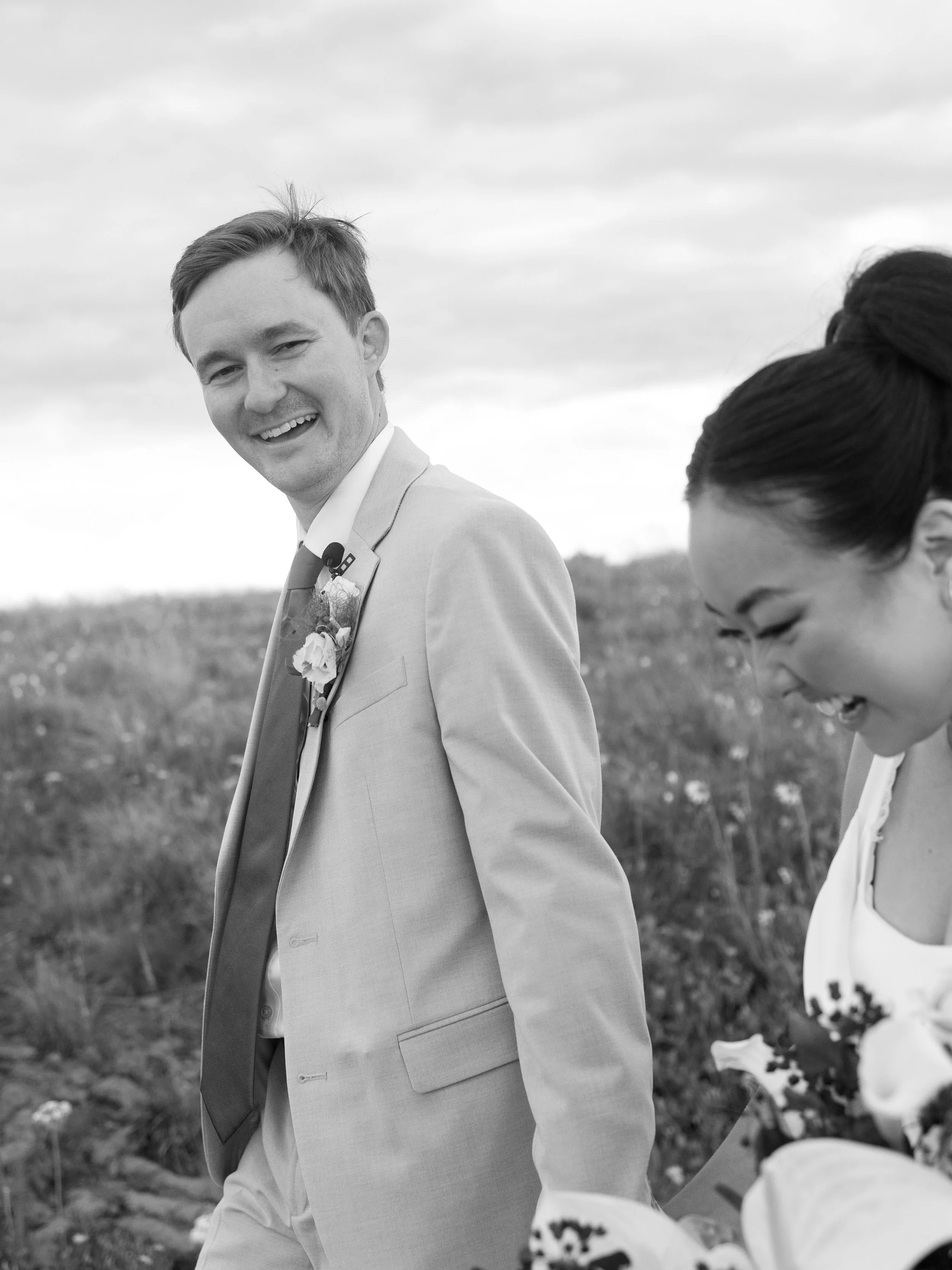 A black and white photo of a smiling man in a suit and a woman laughing outdoors in a field.