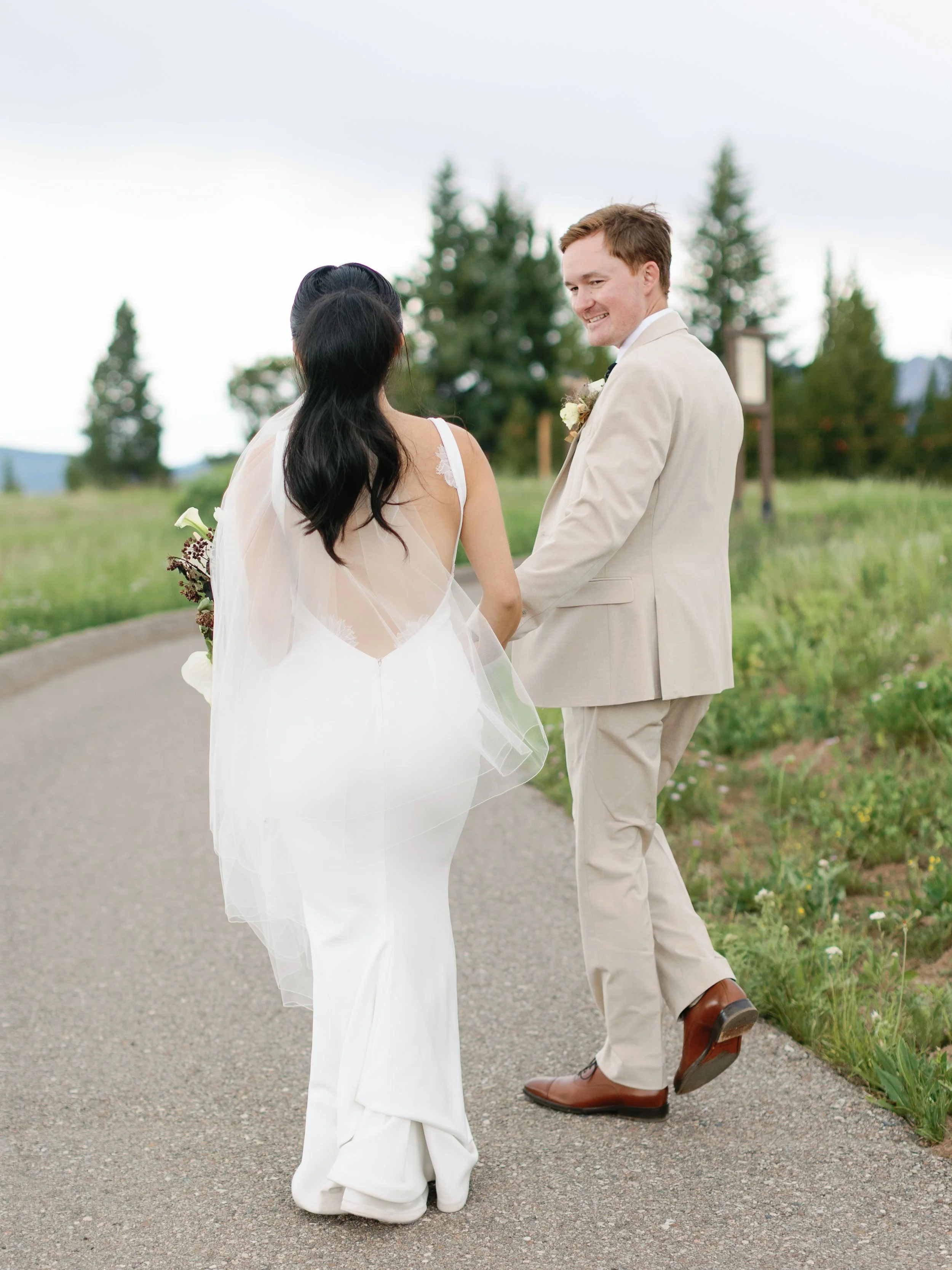 A bride and groom walking on a country road, holding hands, with trees in the background during a wedding ceremony.
